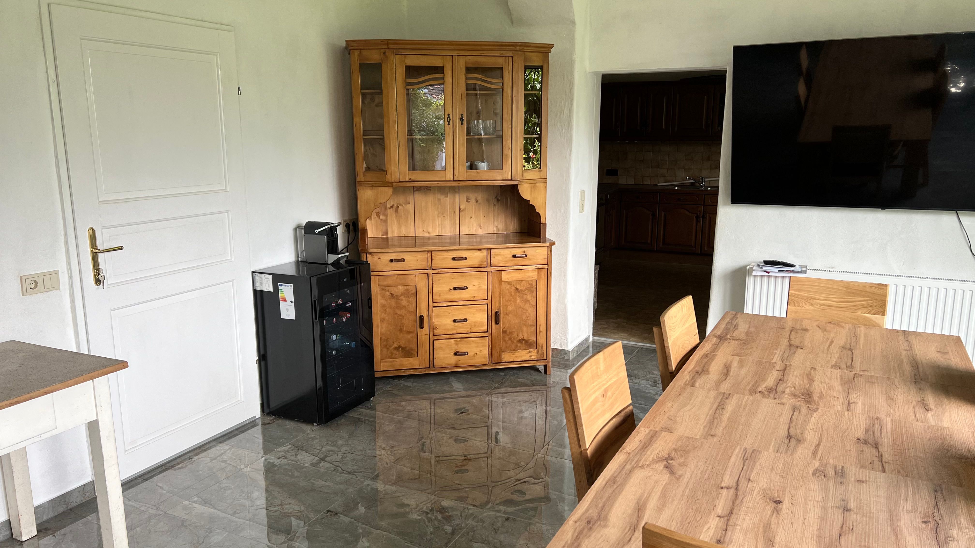 Esszimmer mit Holztisch, Stühlen, Vitrine, Kühlschrank und großem Fernseher an der Wand.
