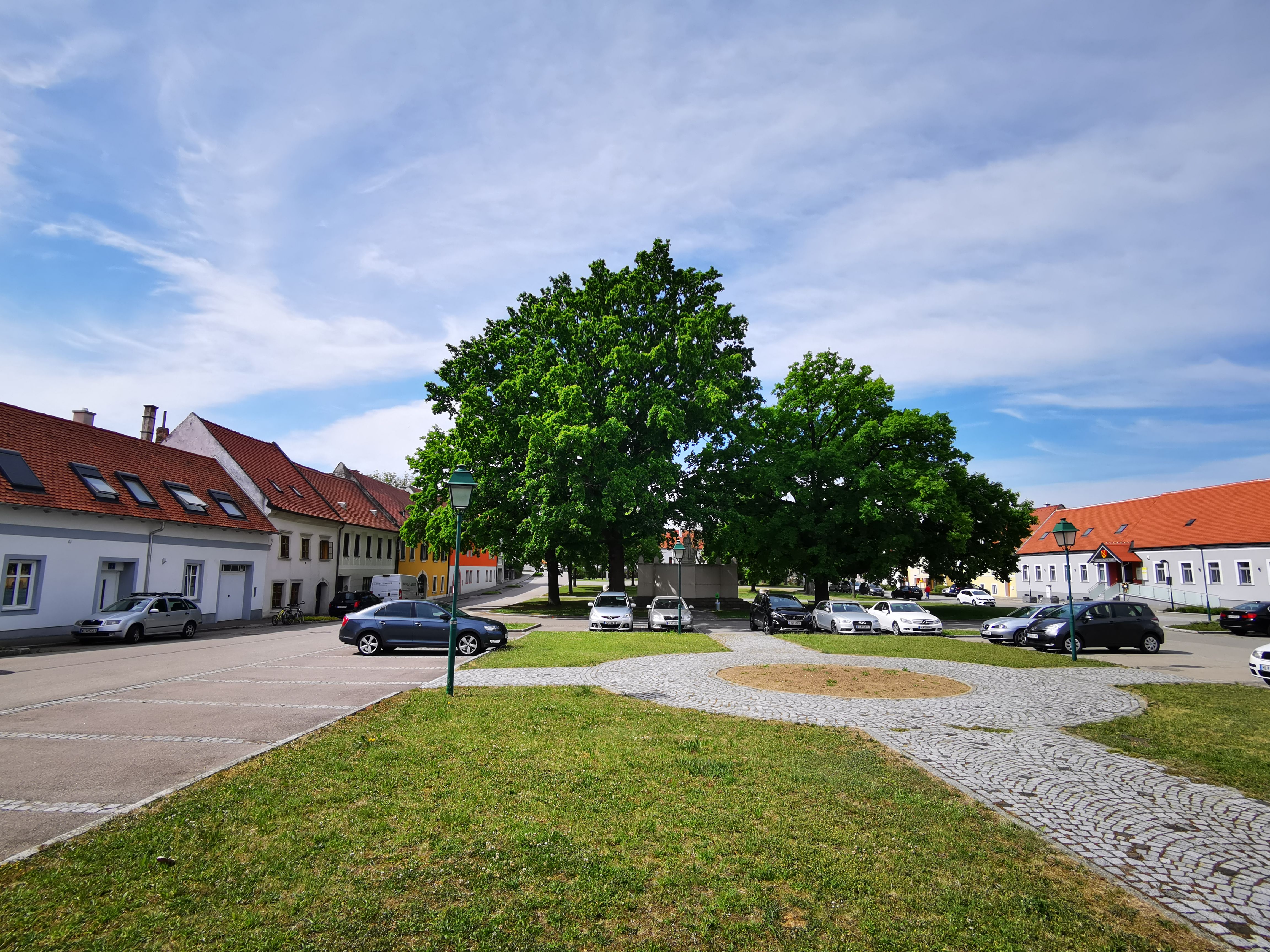 Hauptplatz in Sitzendorf an der Weinstraße mit parkenden Autos und Bäumen.