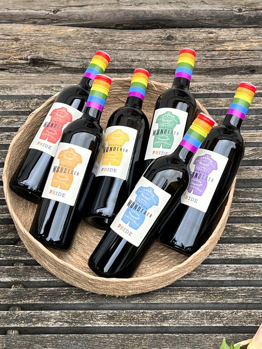 Six wine bottles with rainbow labels in a basket on a wooden table.