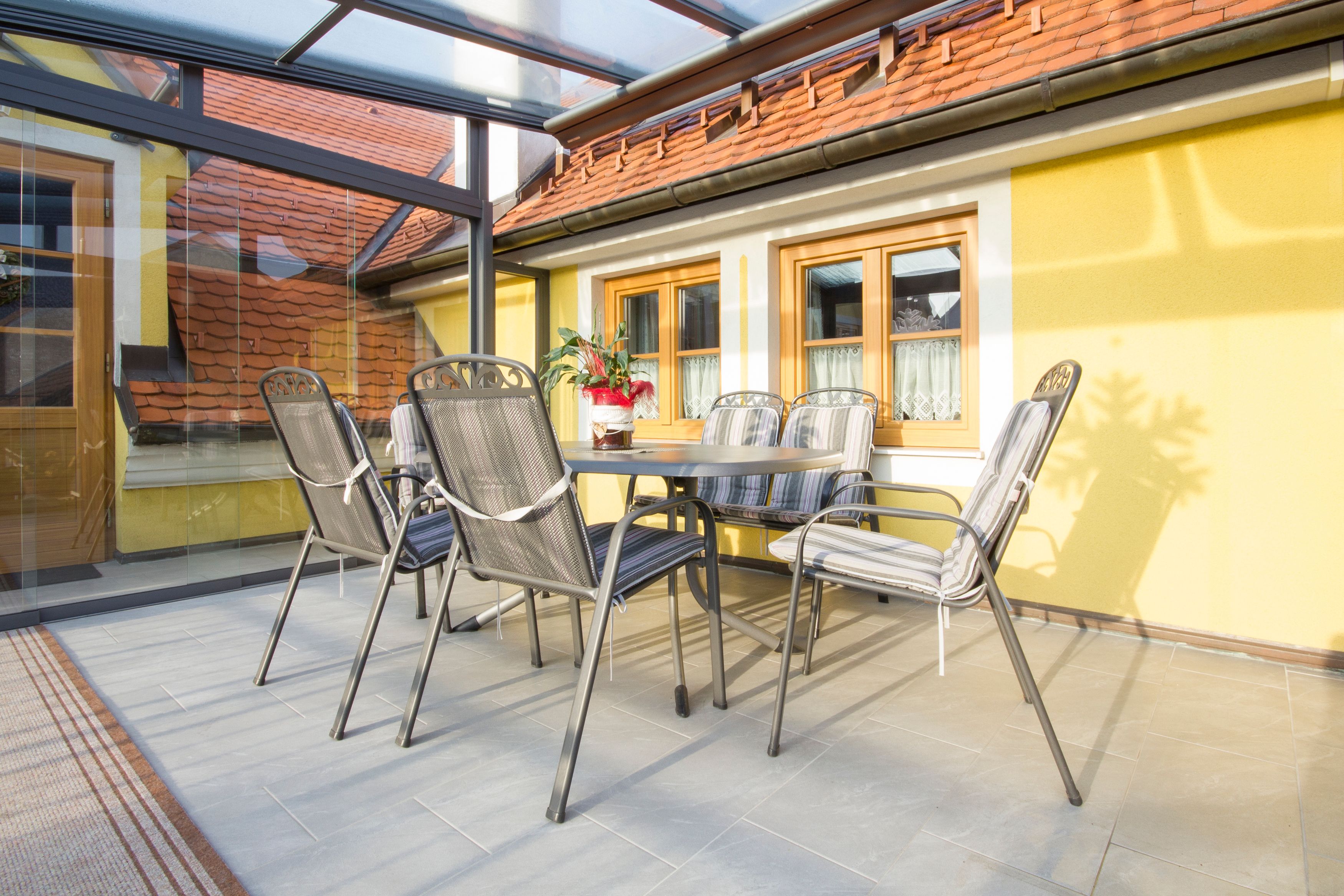 Wintergarten mit Tisch und Stühlen, gelbe Wände, Glasdach.