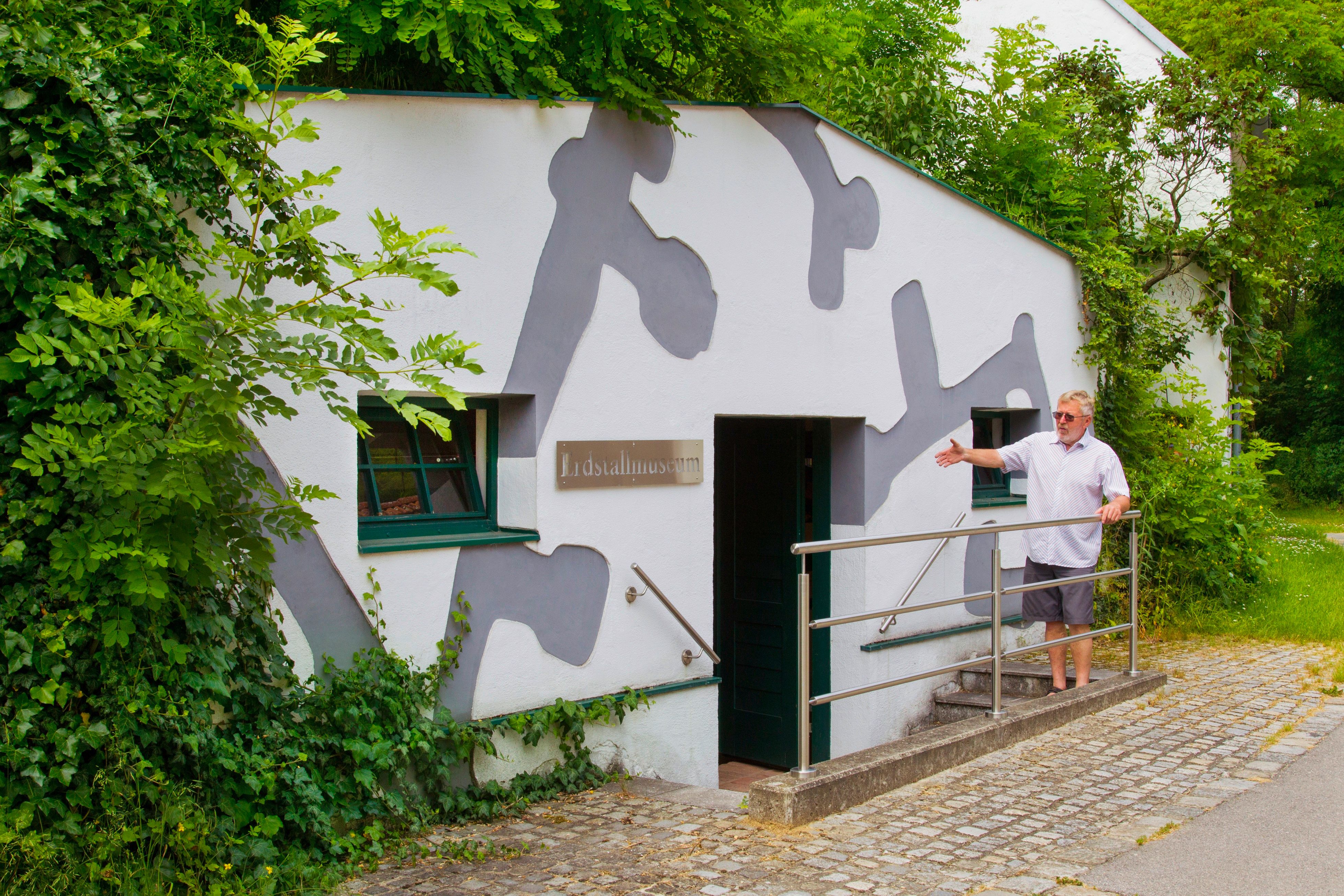Eingang des Erdstallmuseums Althöflein mit einem Mann, der die Tür zeigt.