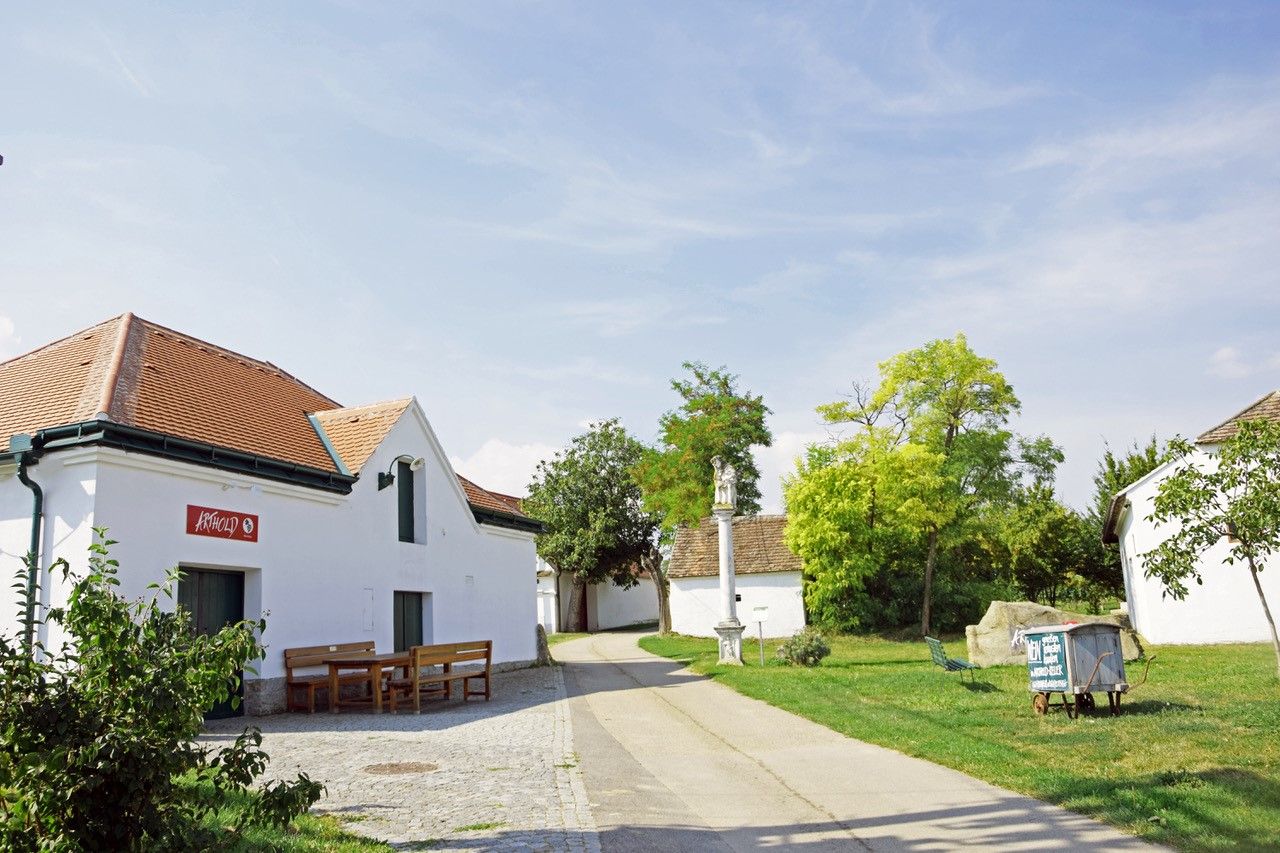 Wine cellar lane with white building and benches in front of a winery on a sunny day.
