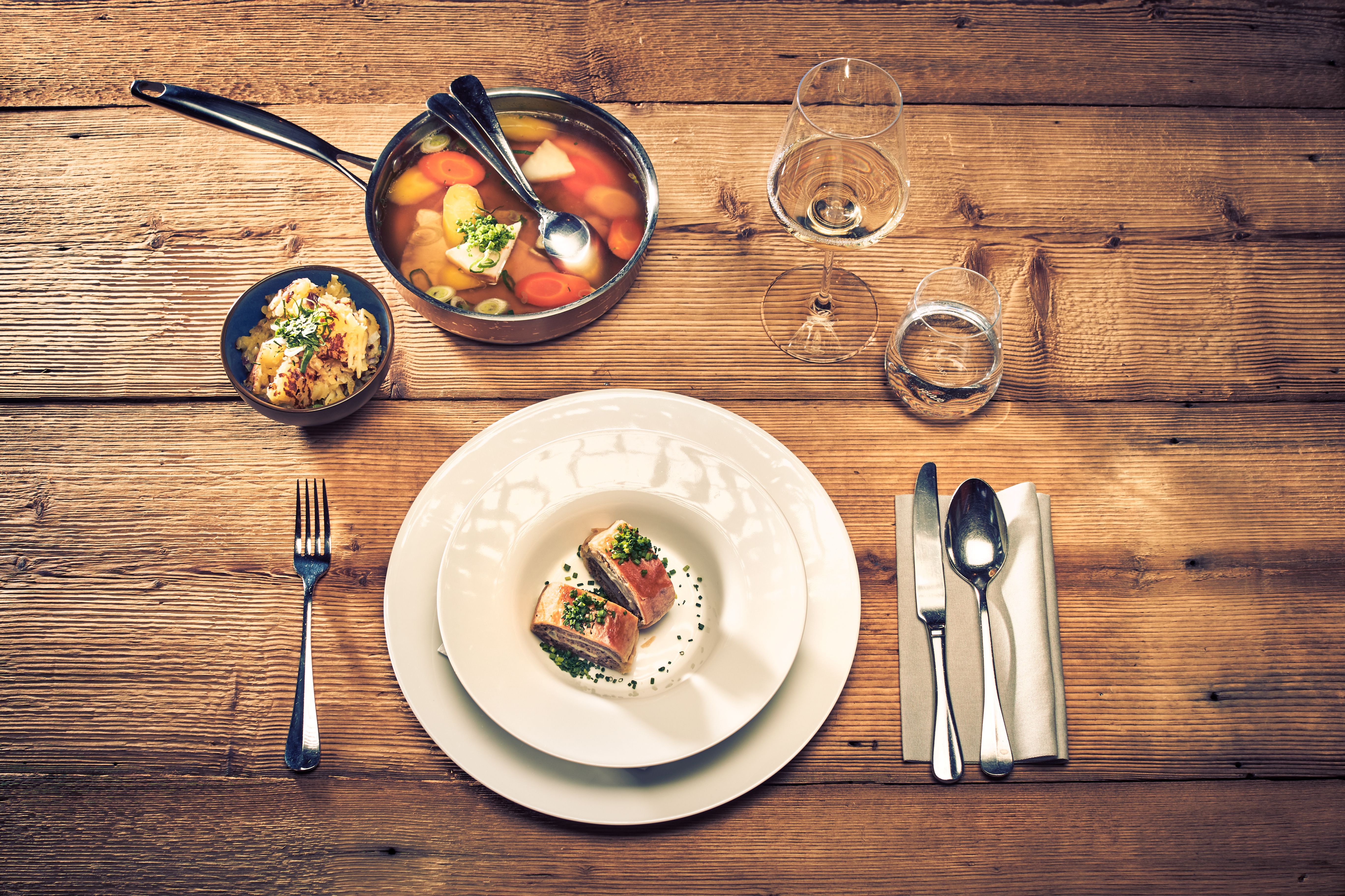 Ein einladender Tisch ist liebevoll gedeckt und verspricht ein köstliches Erlebnis. Der Duft von frisch zubereitetem Tafelspitz und einer herzhaften Suppe erfüllt die Luft, während die sanfte Holzmaserung des Tisches eine warme Atmosphäre schafft. Hier wird die Wirtshauskultur lebendig und lädt zum Verweilen ein.