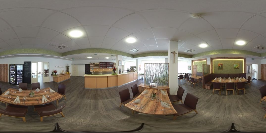 Interior view of a modern restaurant with wooden tables and chairs, decorated with plants and works of art on the walls.