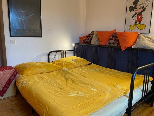 Schlafzimmer mit gelber Bettwäsche, Poster an der Wand und Kissen auf dem Bett.