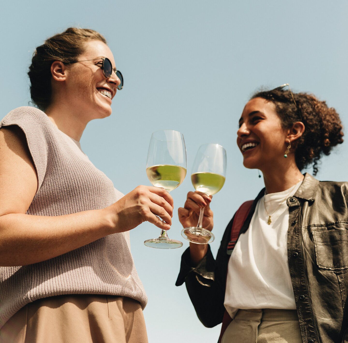 Zwei Freundinnen stoßen mit Gläsern voll erfrischendem Wein an und genießen die strahlende Sonne. Umgeben von sanften Hügeln und üppigen Weinreben, strahlt die Atmosphäre Freude und Entspannung aus. Der Weinherbst lädt dazu ein, die köstlichen Aromen der Region zu entdecken.