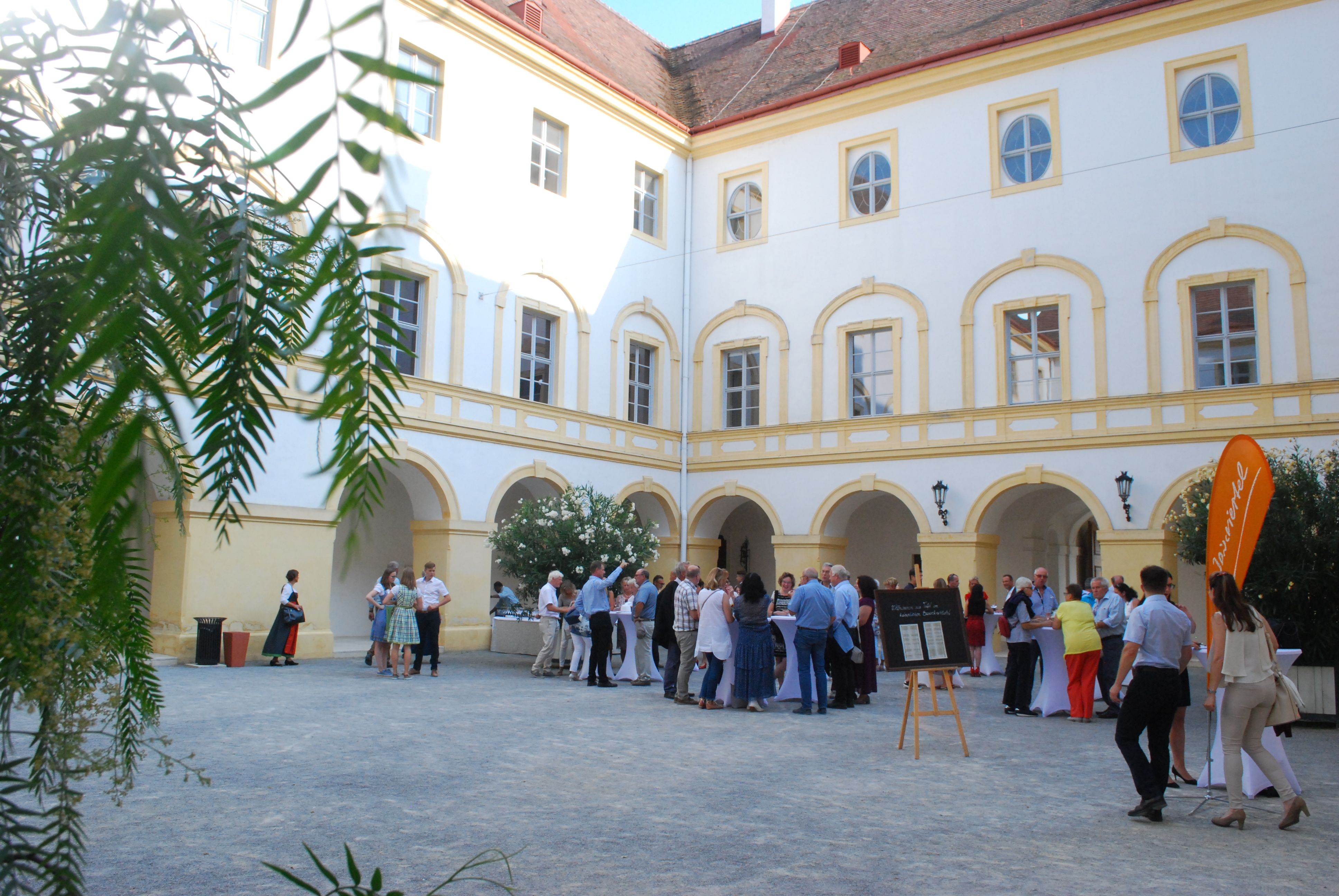 Menschen versammeln sich in einem historischen Schlosshof mit gelb-weißen Fassaden.