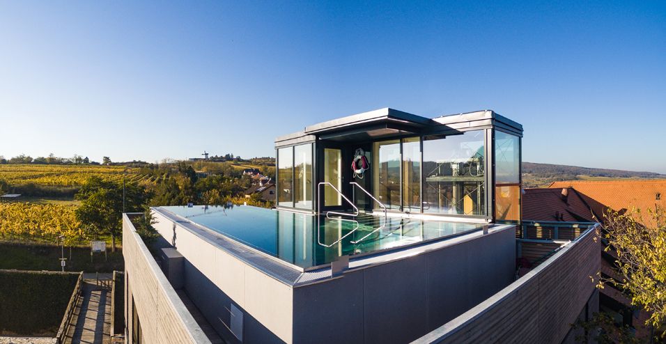 Ein moderner Dachpool mit Glaswänden und Blick auf eine herbstliche Landschaft mit Weinbergen.