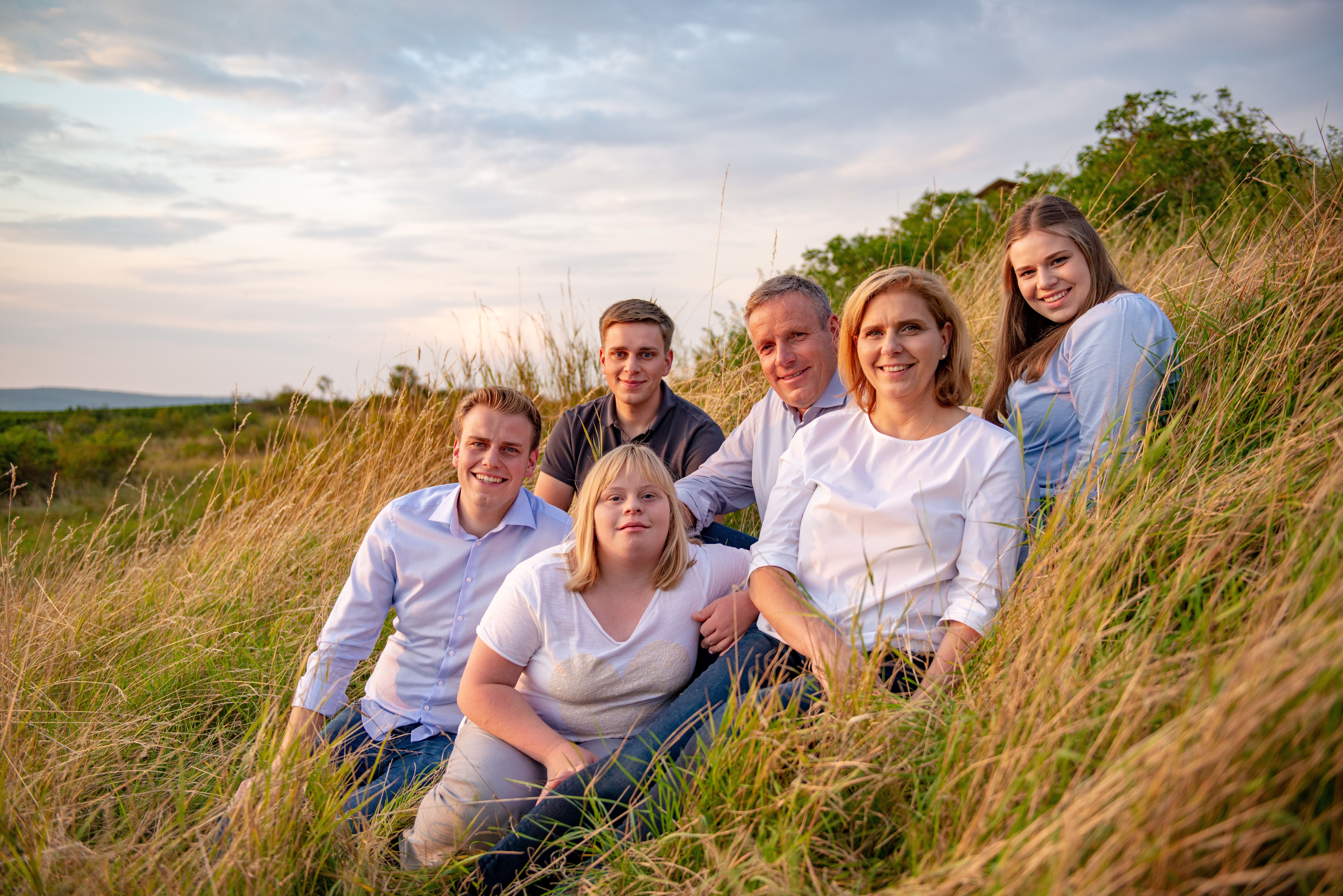 Eine Gruppe von sechs Personen sitzt in einem Feld bei Sonnenuntergang.