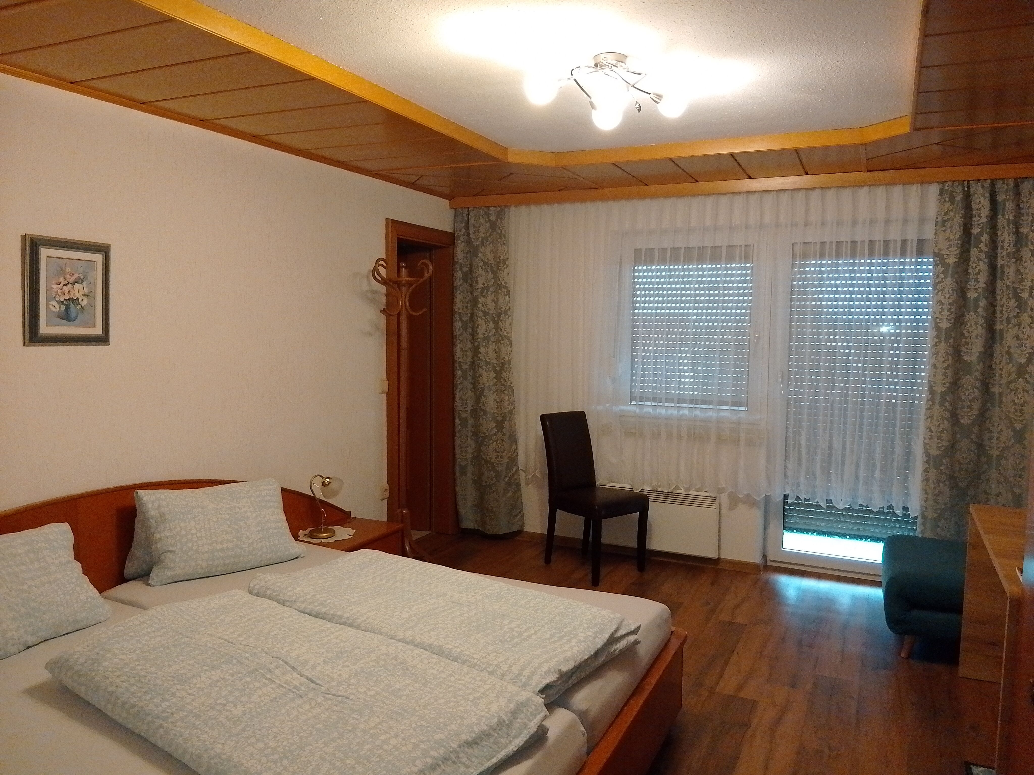 Ein gemütliches Schlafzimmer mit Doppelbett, Holzdecke, Vorhängen und einem Stuhl vor einem Fenster.