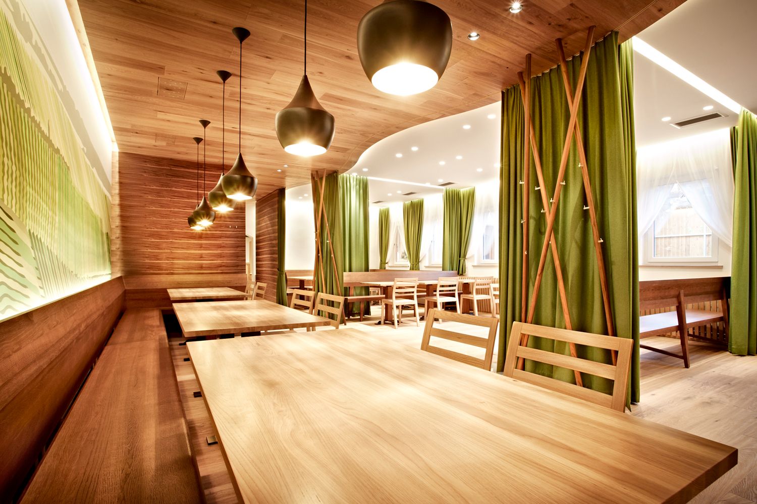 Modernes Restaurant mit Holztischen und grünen Vorhängen.