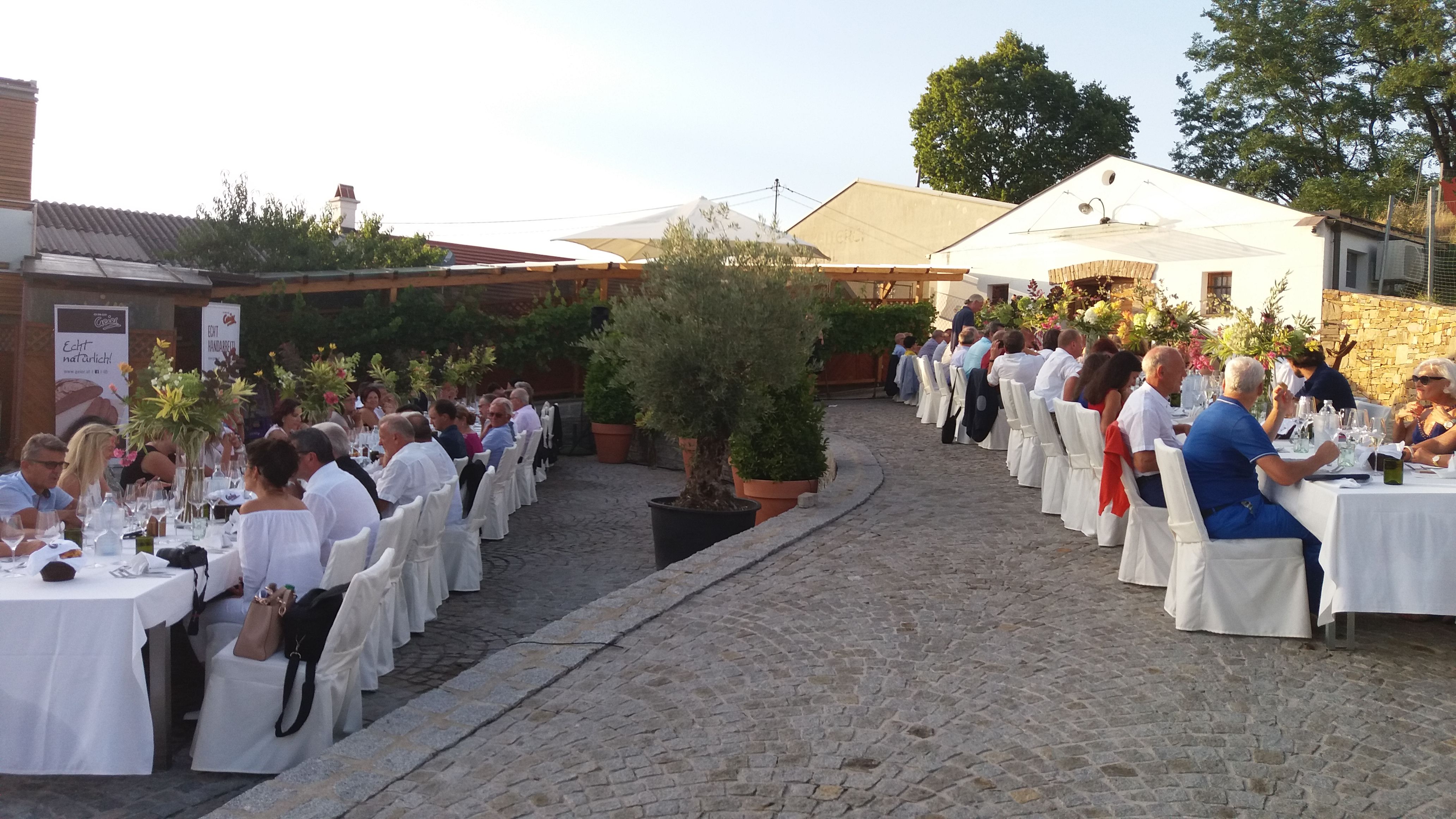 Menschen sitzen an langen, festlich gedeckten Tischen im Freien.
