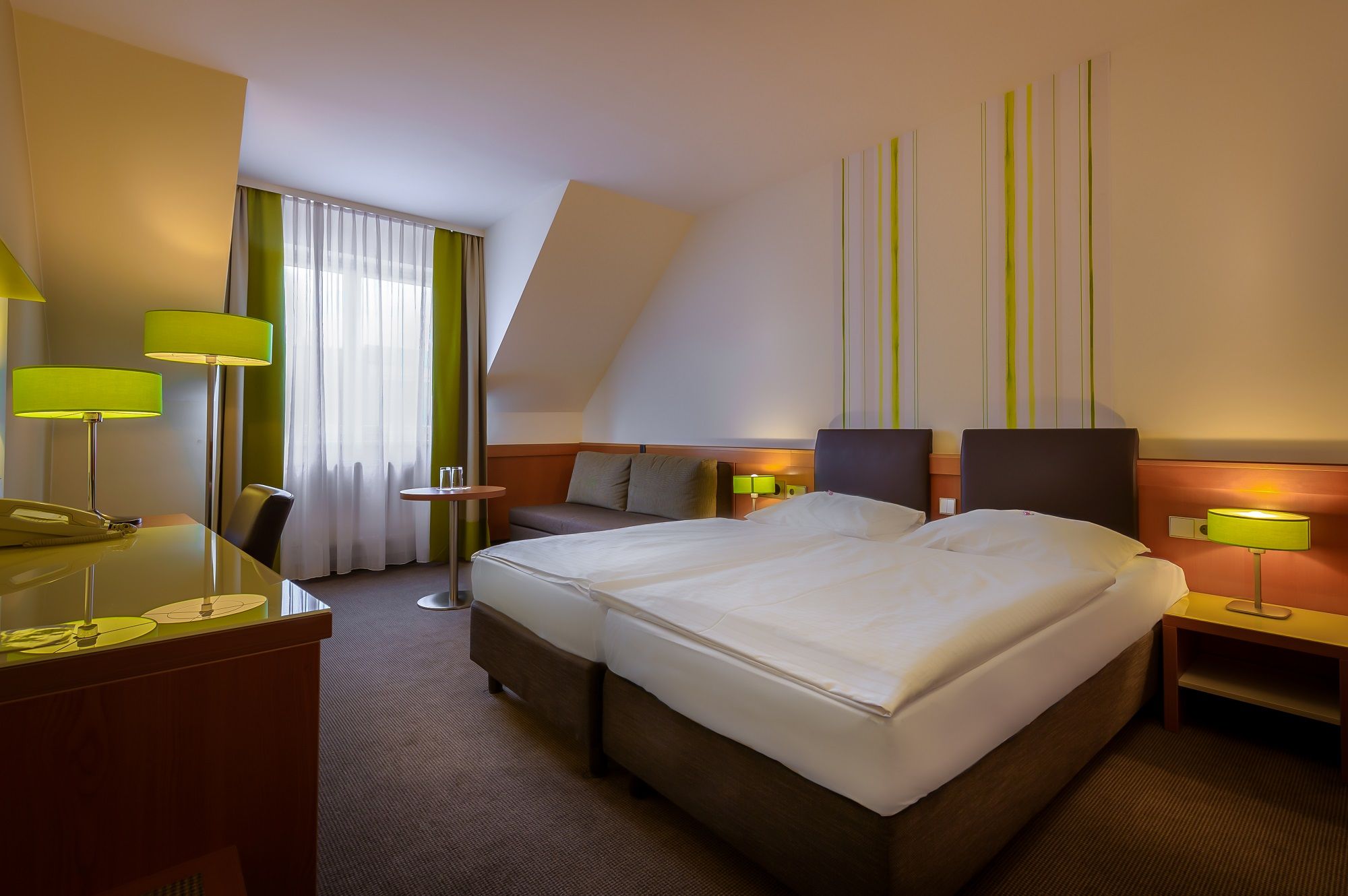 Modern hotel room with two beds, desk and green lamps.