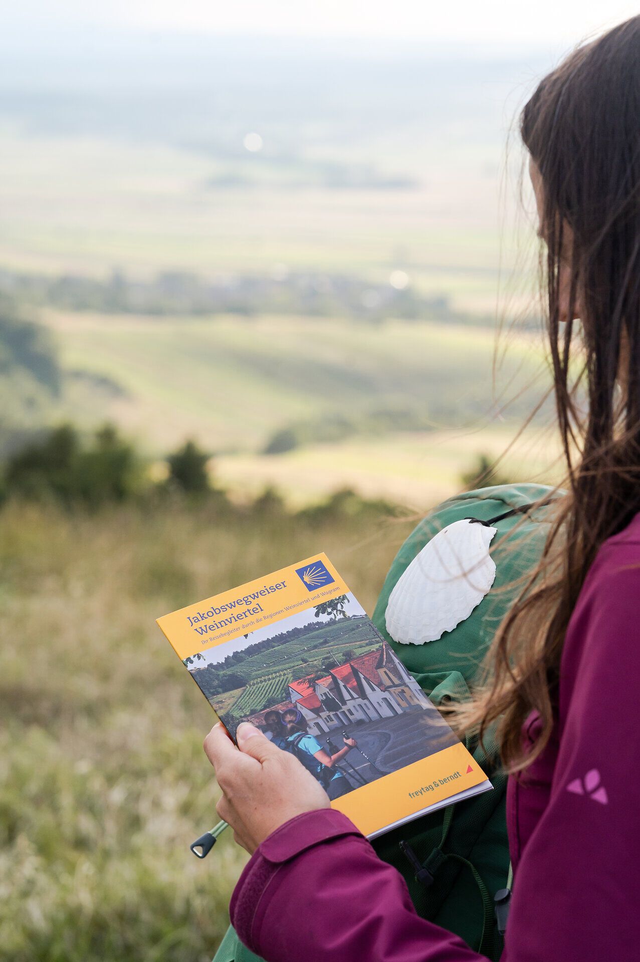 Eine Wanderin hält ein Reisehandbuch zum Jakobsweg Weinviertel in der Hand.