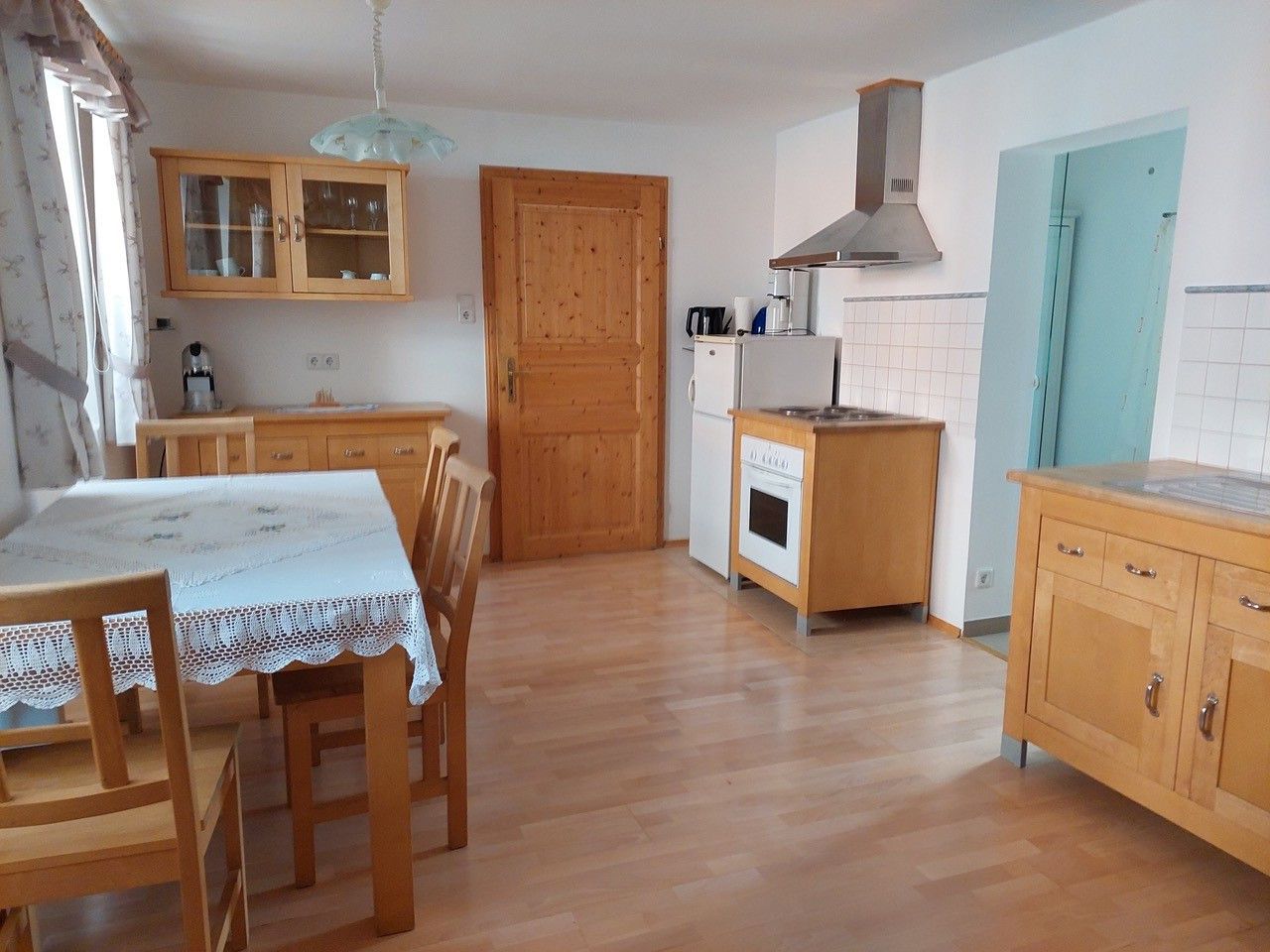 Wohnküche mit Holzmöbeln, Esstisch, Stühlen, Herd, Kühlschrank und Hängeschrank.