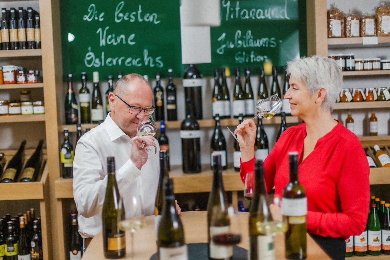 Zwei Personen verkosten Wein in einem Geschäft mit Weinflaschen im Hintergrund.