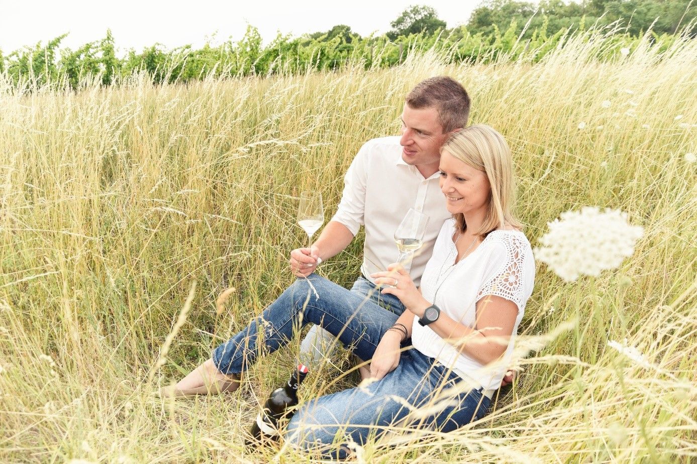 Ein Paar sitzt im hohen Gras und trinkt Wein.