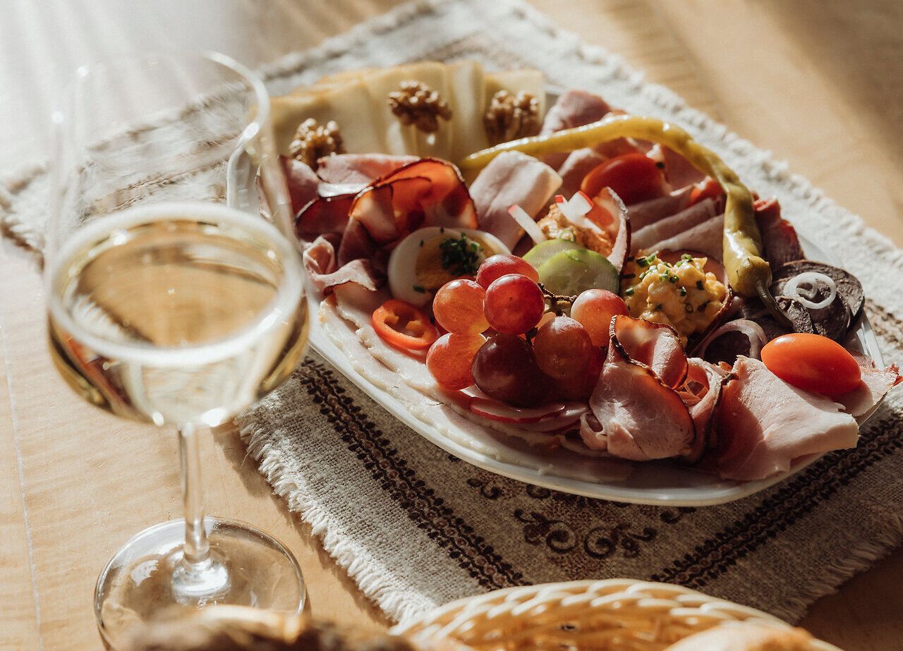 Genießen Sie die köstliche Brettljause, die mit frischen regionalen Zutaten zubereitet wurde, während Sie in entspannter Atmosphäre ein Glas Wein nippen. Die warmen Sonnenstrahlen tauchen die Tafel in ein goldenes Licht und laden dazu ein, die Schönheit der Weinviertler Heurigenkultur zu erleben.
