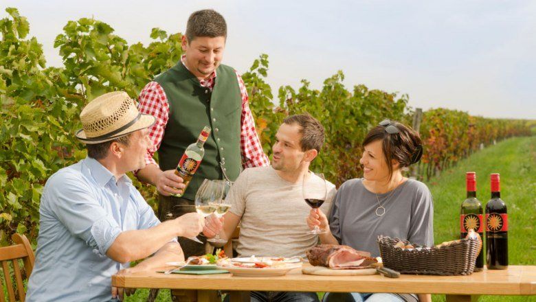 Menschen genießen Wein und Essen im Freien in einem Weinberg.