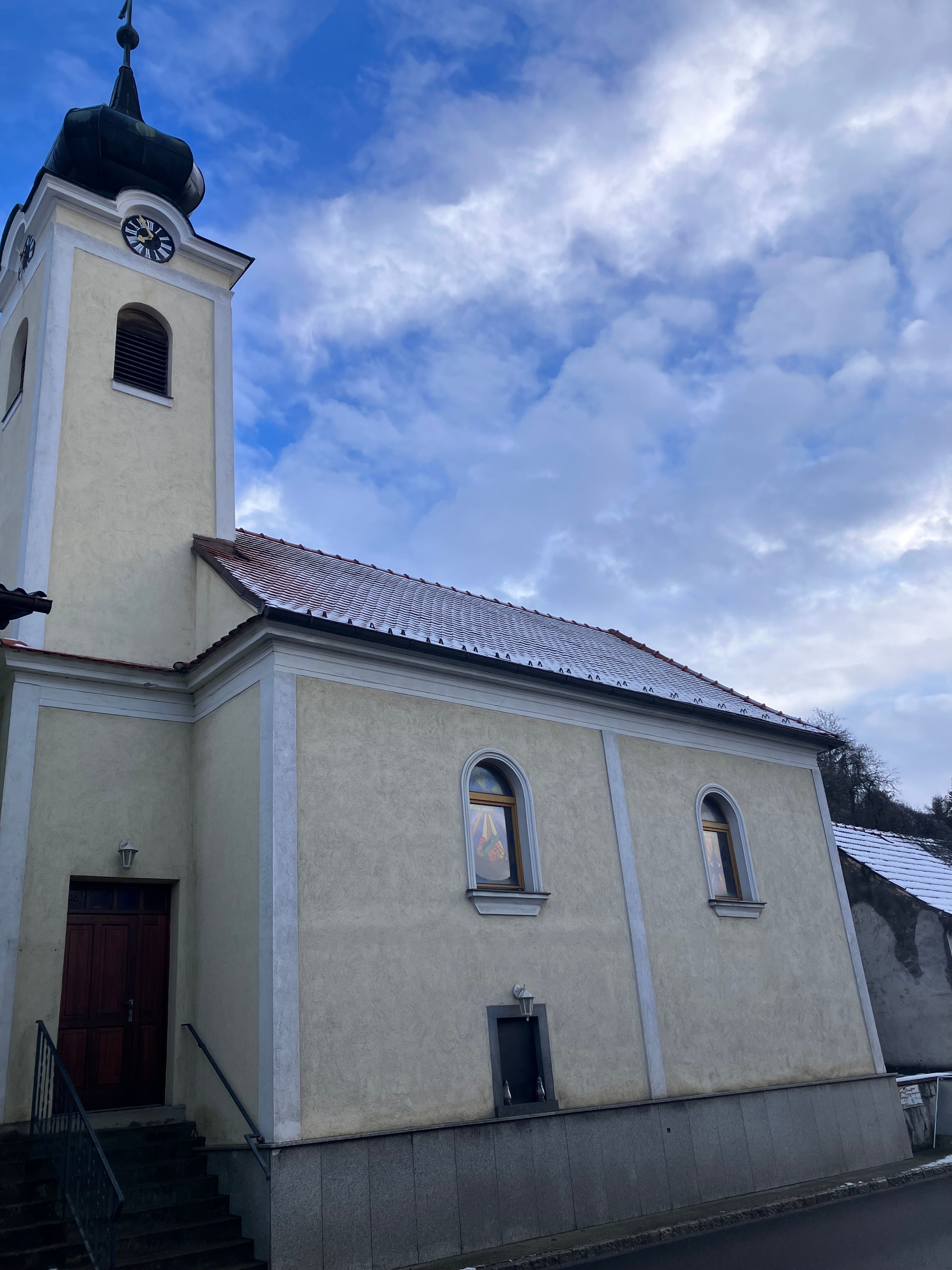 Kirche mit Turm und Uhr vor bewölktem Himmel.