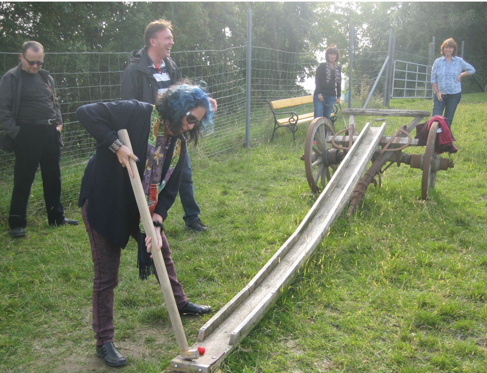 Person spielt Bauerngolf mit einem Holzschläger auf einer Wiese.