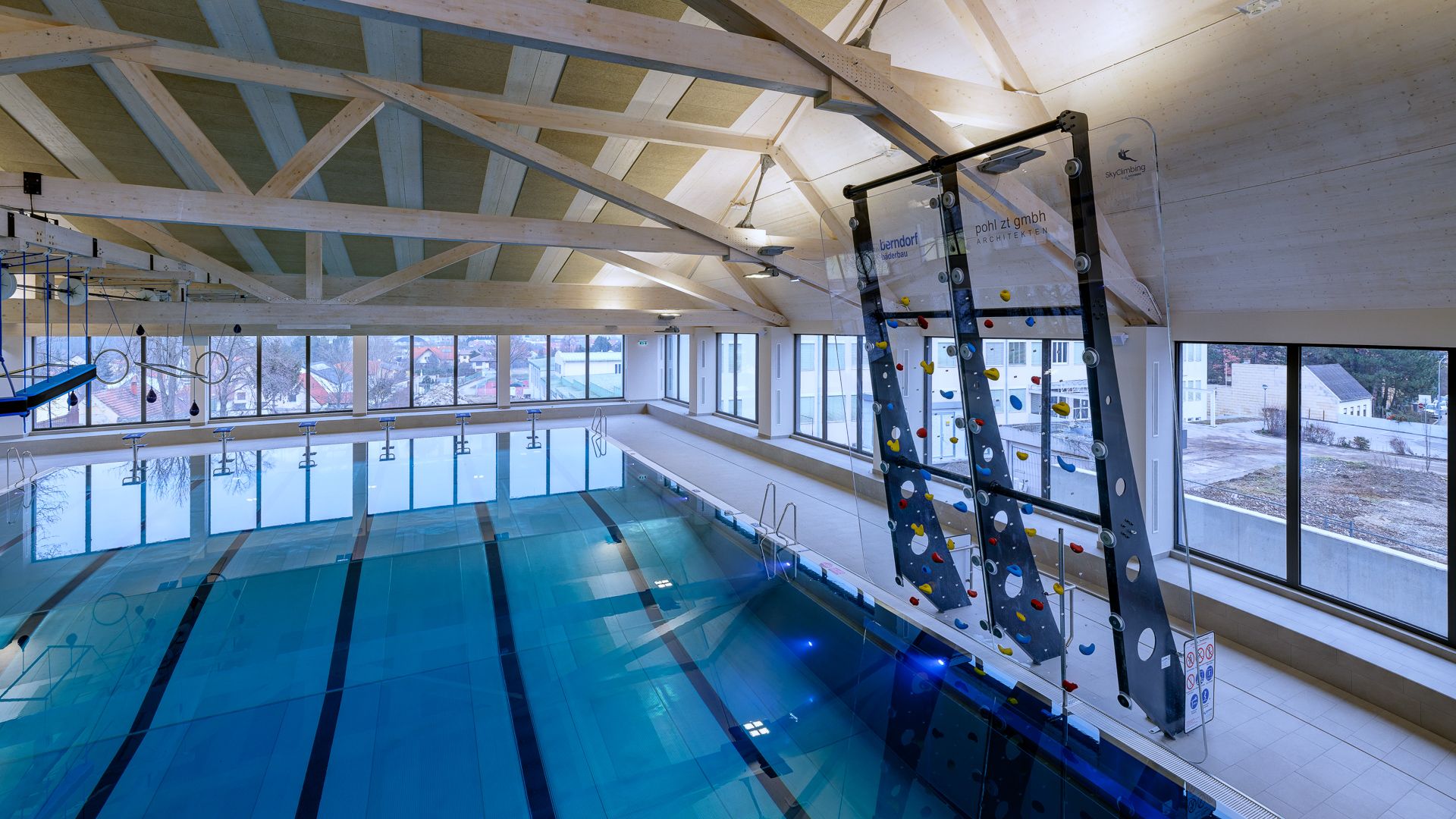 Innenansicht eines Schwimmbads mit Kletterwand und großen Fenstern.