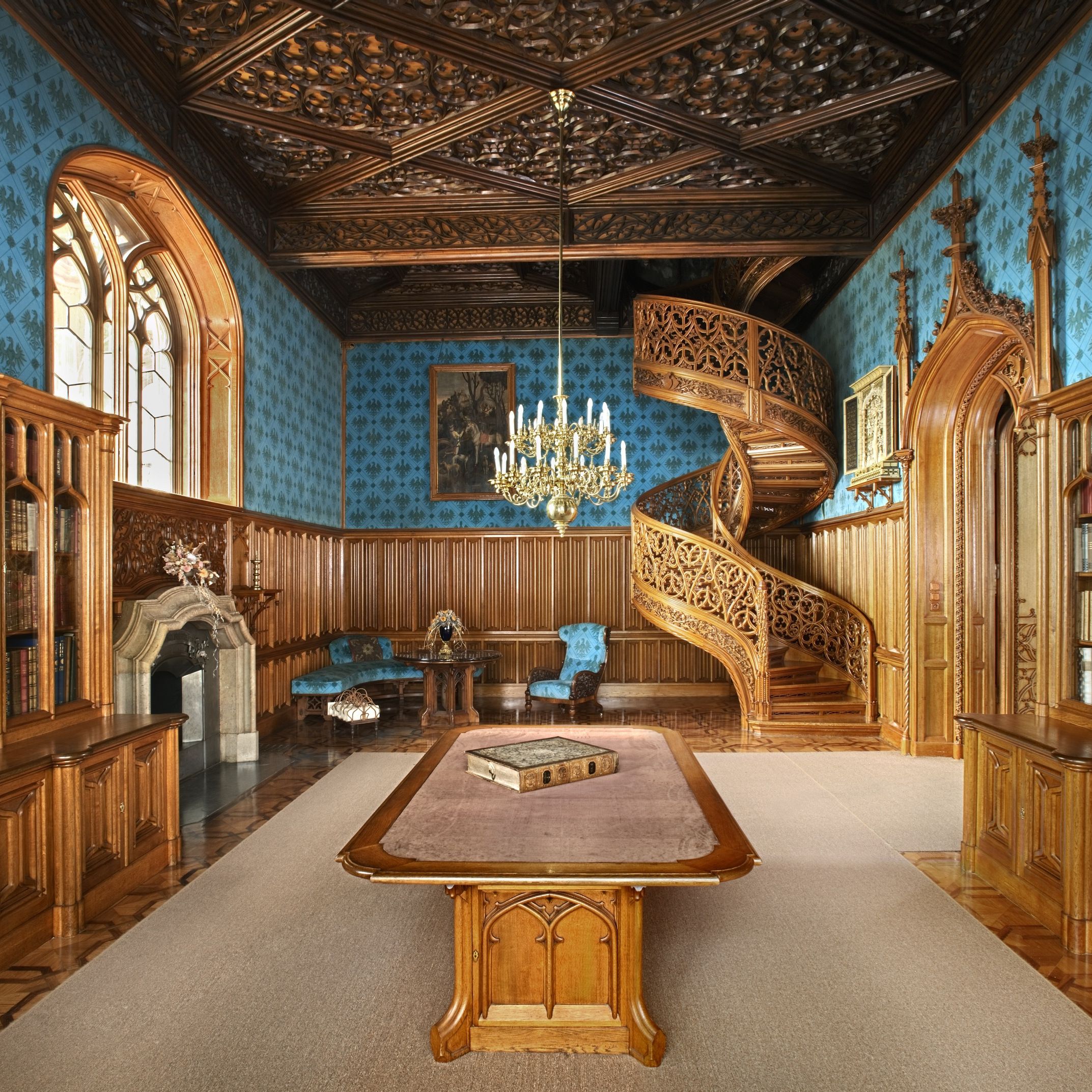 Innenansicht eines prächtigen Raumes im Schloss Lednice mit einer kunstvoll geschnitzten Wendeltreppe und einem großen Tisch in der Mitte.