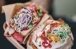 Eine Person hält zwei Winzerweckerl, gefüllt mit regionalen Produkten wie frischem Gemüse, Sauerkraut und mehr, in die Kamera. 