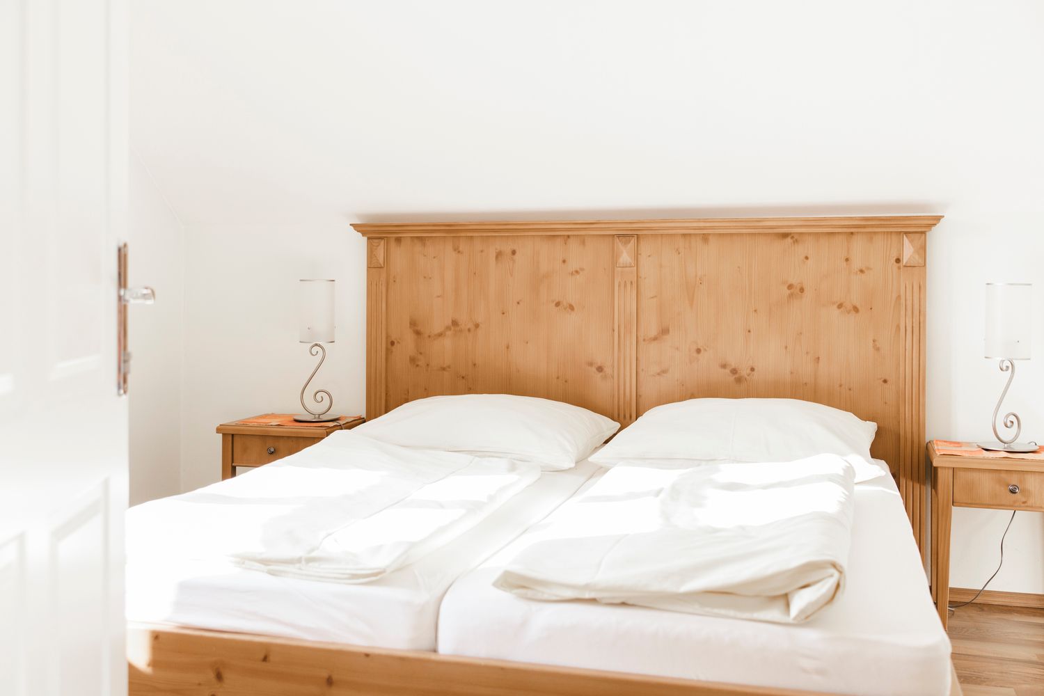 Helles Schlafzimmer mit einem Doppelbett aus Holz und weißen Bettlaken.