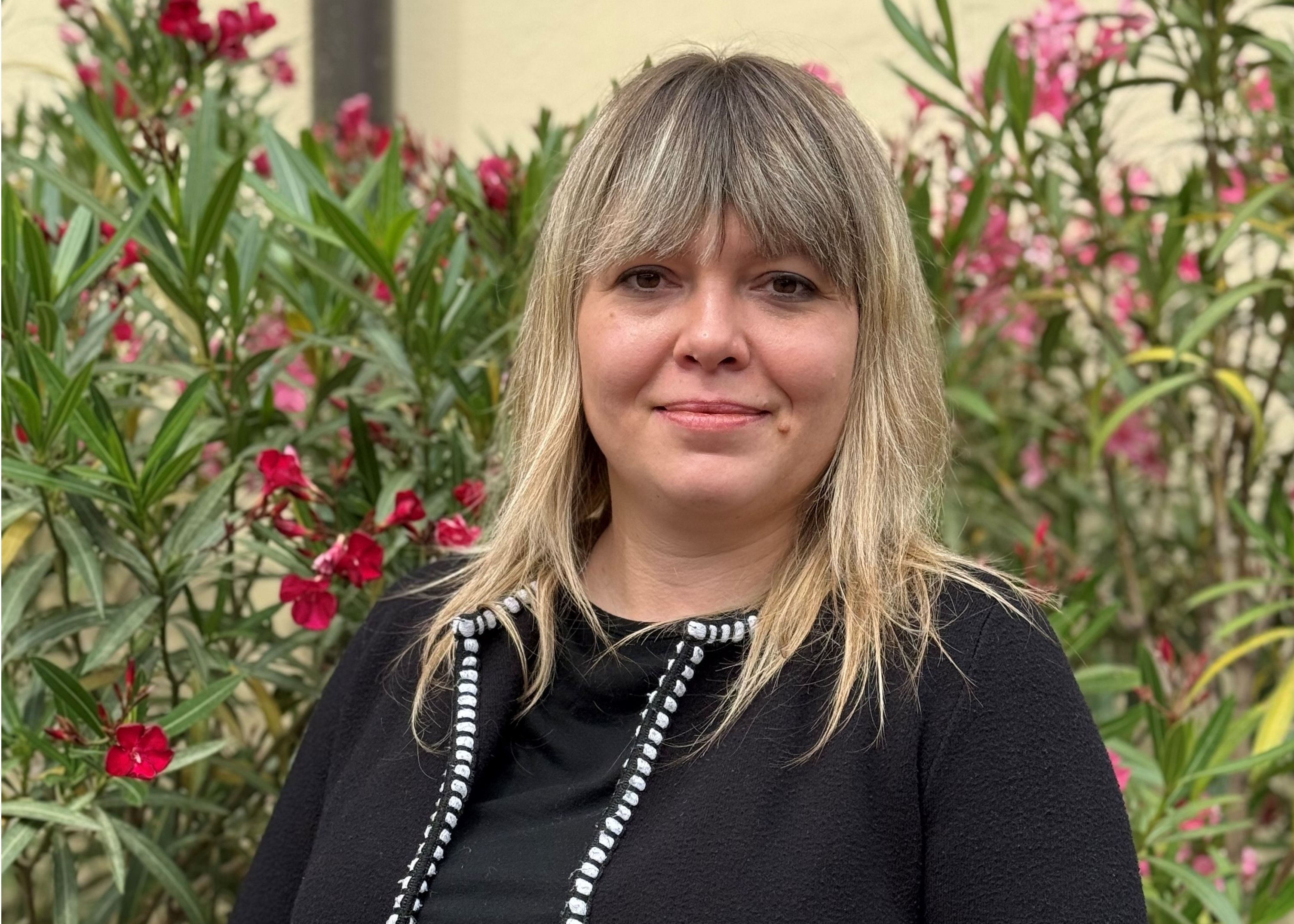 Eine Frau mit blonden Haaren steht vor blühenden Oleandersträuchern.