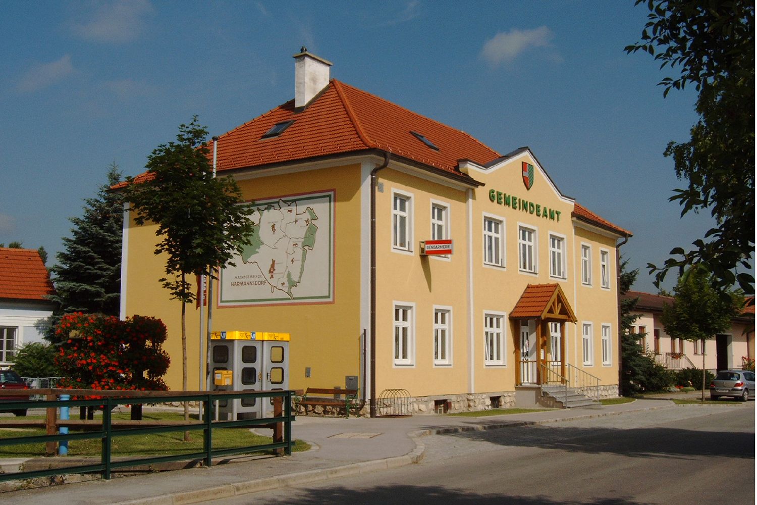Ein gelbes Gebäude mit der Aufschrift 'Gemeindeamt', einem Wappen und einer Karte an der Wand.