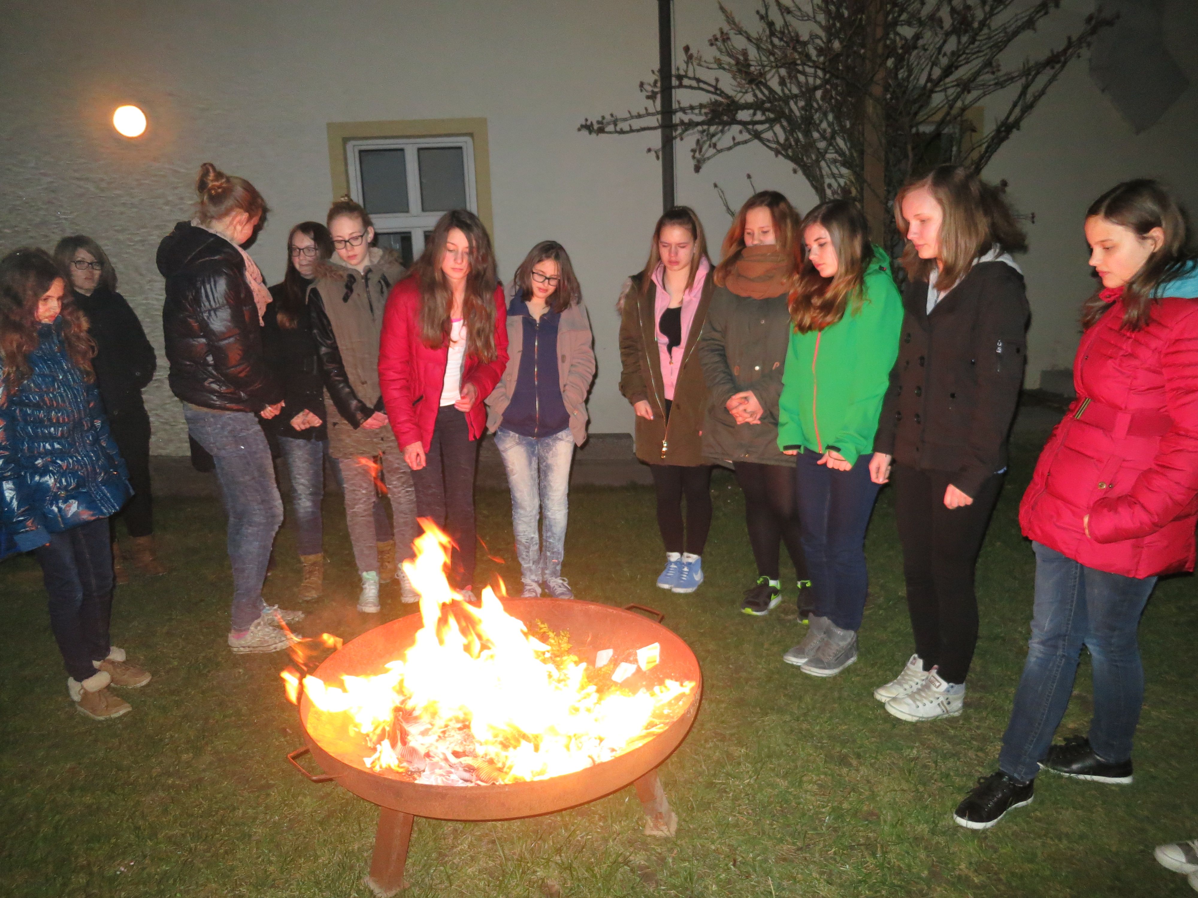 Skupina mladých ľudí stojacich okolo vonkajšieho ohniska.