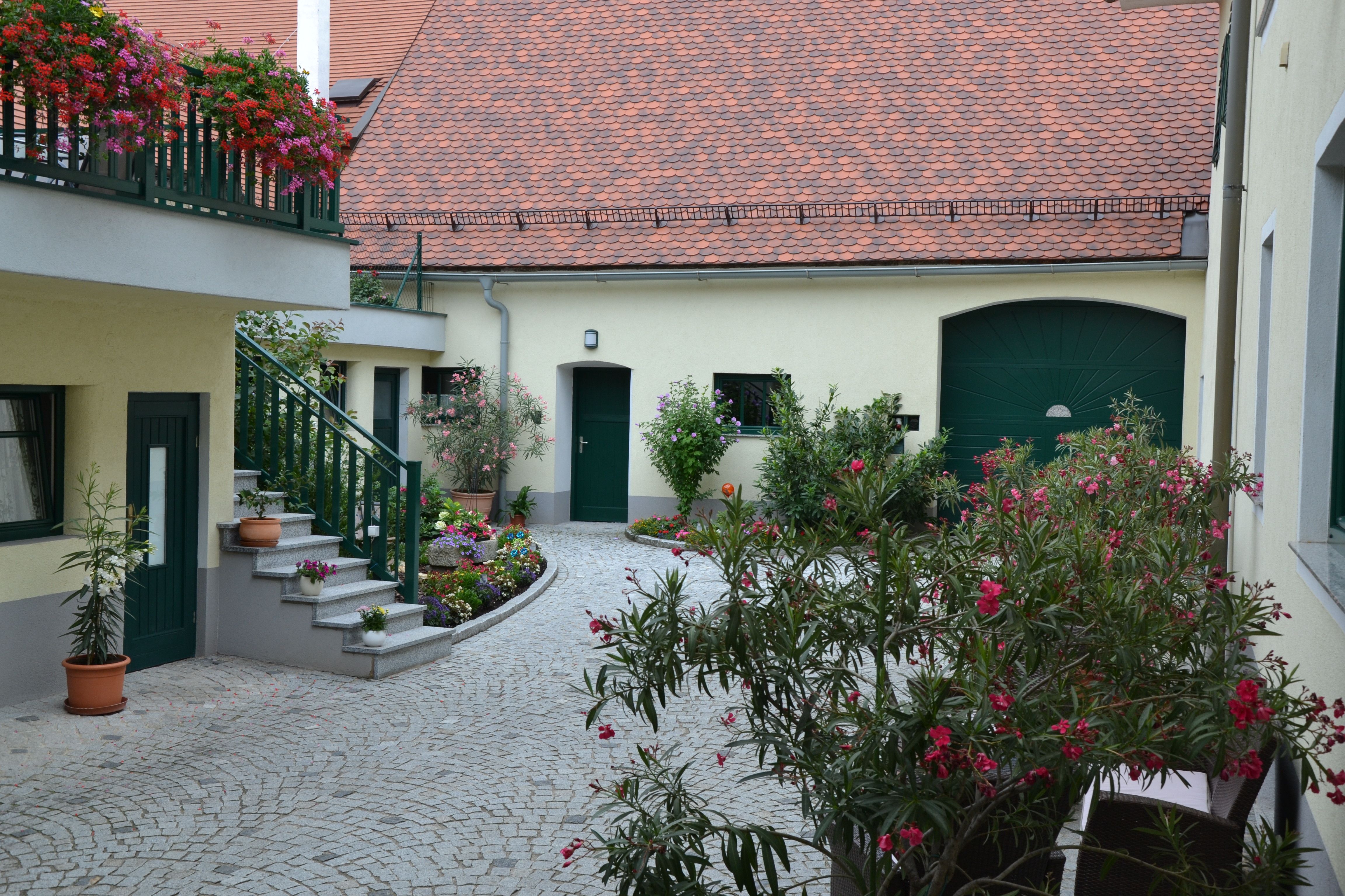 Ein gepflegter Innenhof mit Blumen und Pflanzen, umgeben von Gebäuden mit roten Ziegeldächern und grünen Türen.
