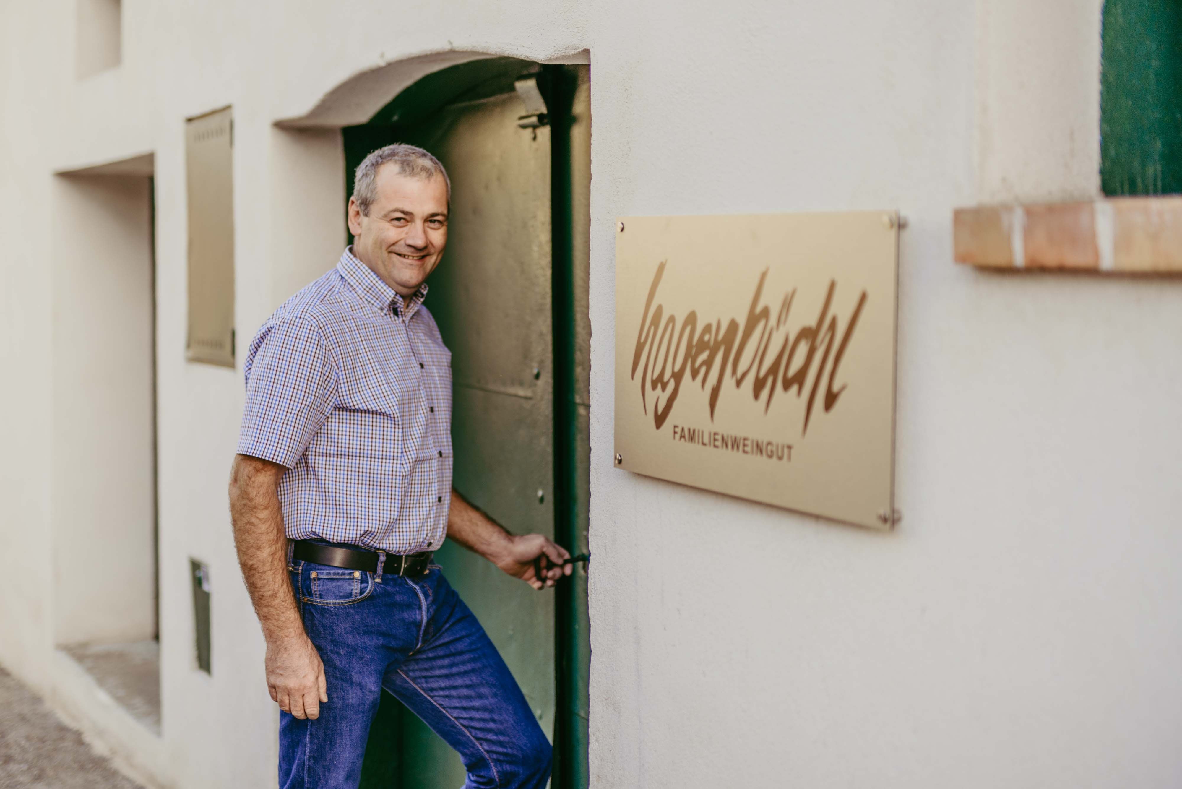A man opens a door next to a sign that reads 'Hagenbüchl Familienweingut'.