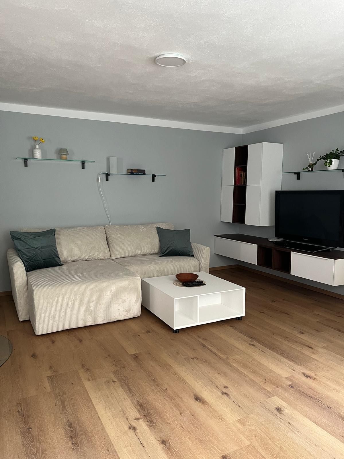 Modernes Wohnzimmer mit beiger Couch, weißem Couchtisch, Holzfußboden und Wandregalen.