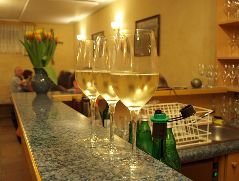 Three wine glasses with white wine on a counter, in the background a vase with tulips.