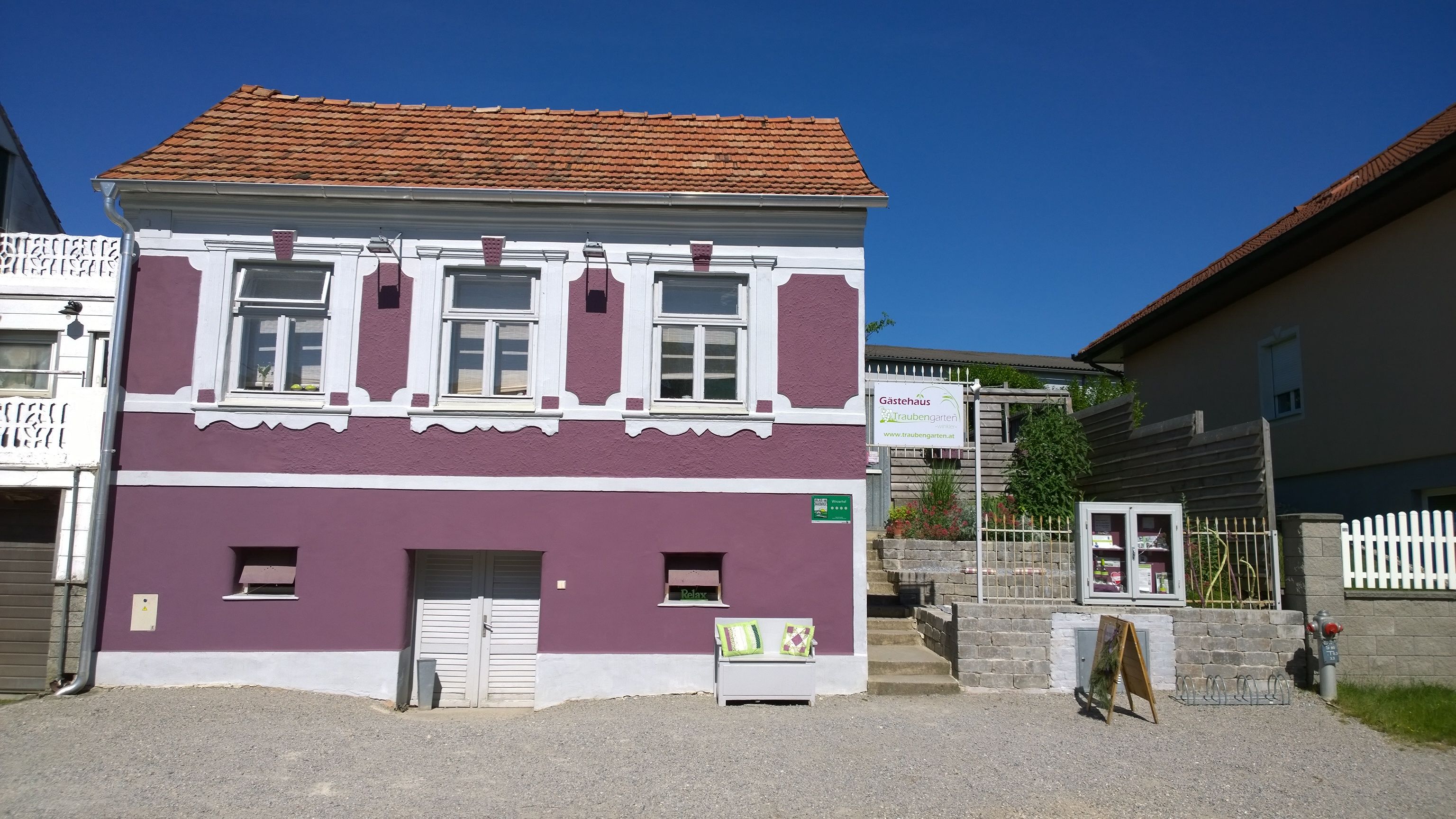 Außenansicht eines lila Hauses mit weißen Fensterrahmen und einem Schild für ein Gästehaus.