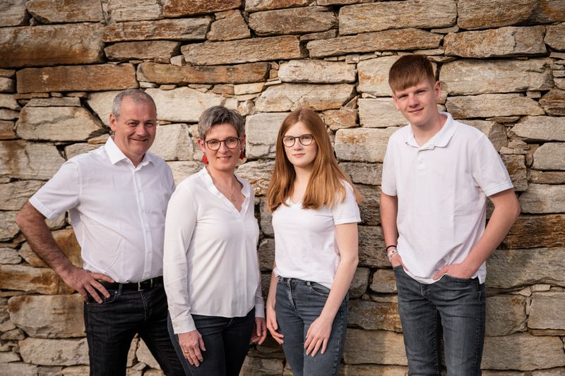 Four people are standing in front of a stone wall, all dressed in white.