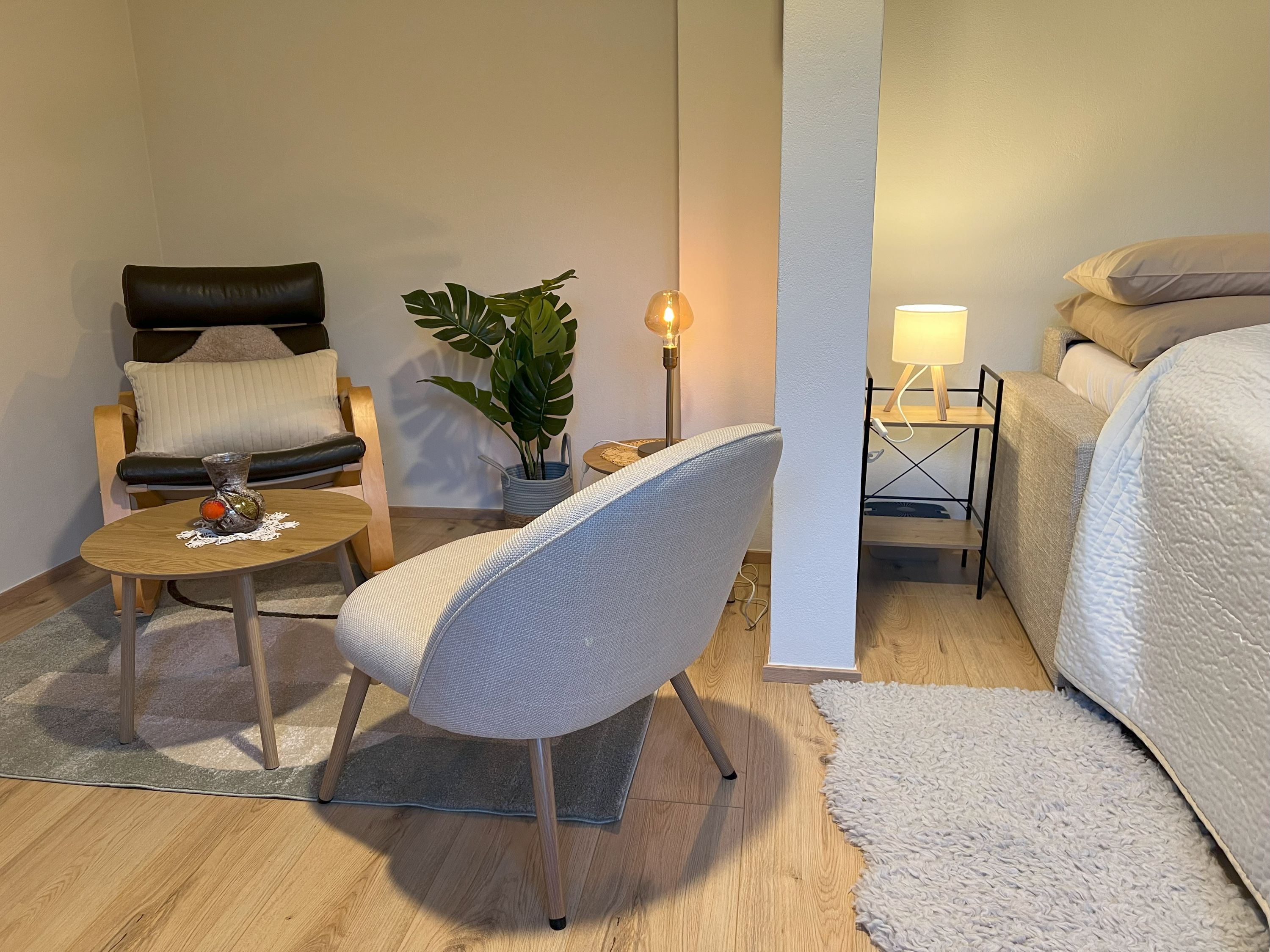 Gemütliches Schlafzimmer mit Sessel, Tisch, Pflanze und Bett.