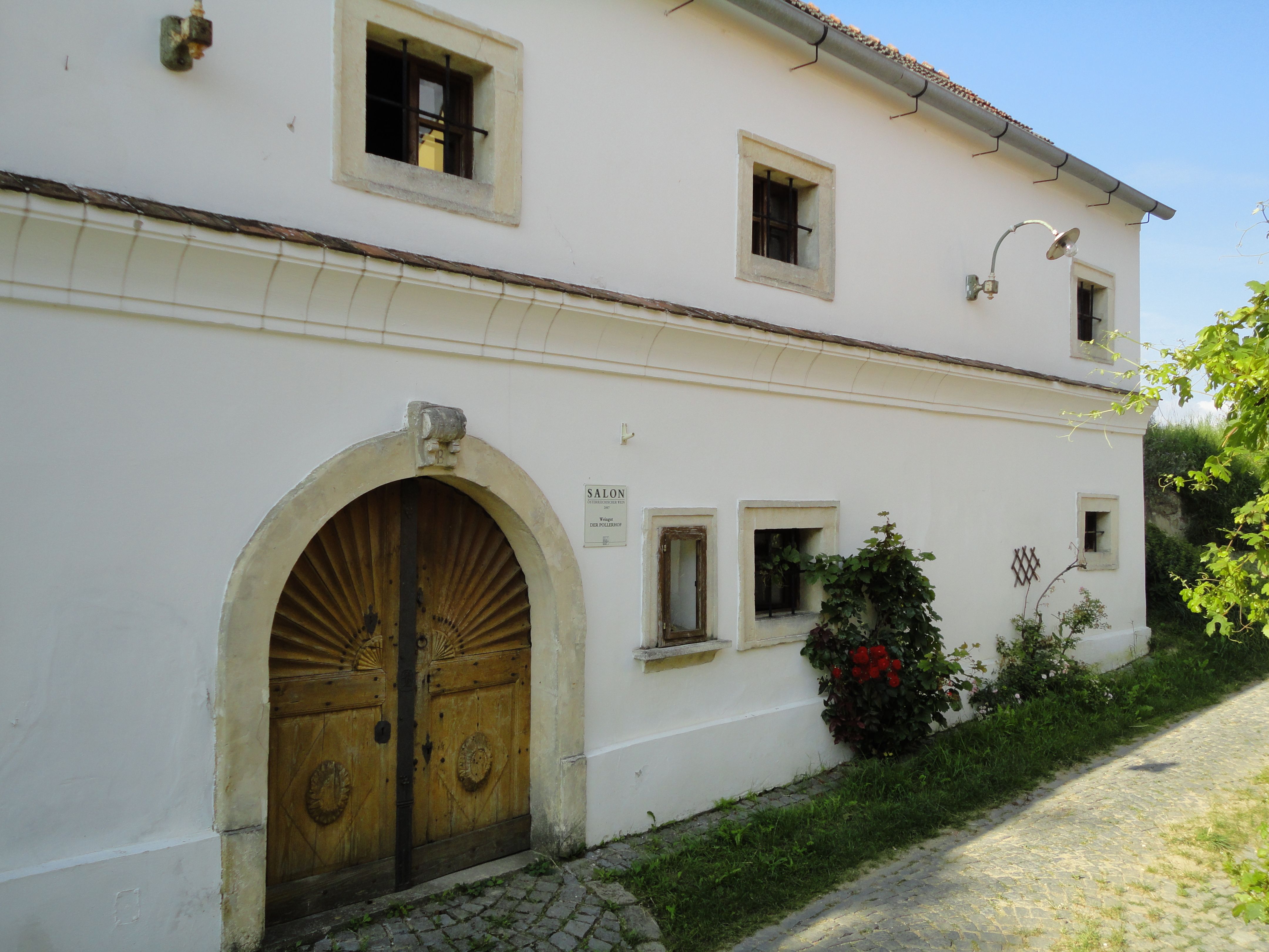 Historic building with wooden door and small windows, surrounded by plants.
