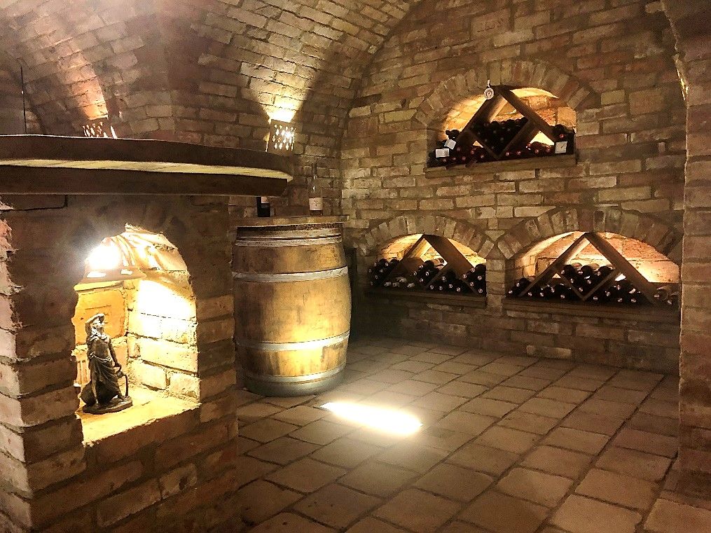 Ein Weinkeller mit Backsteinwänden, Weinregalen und einem Holzfass.
