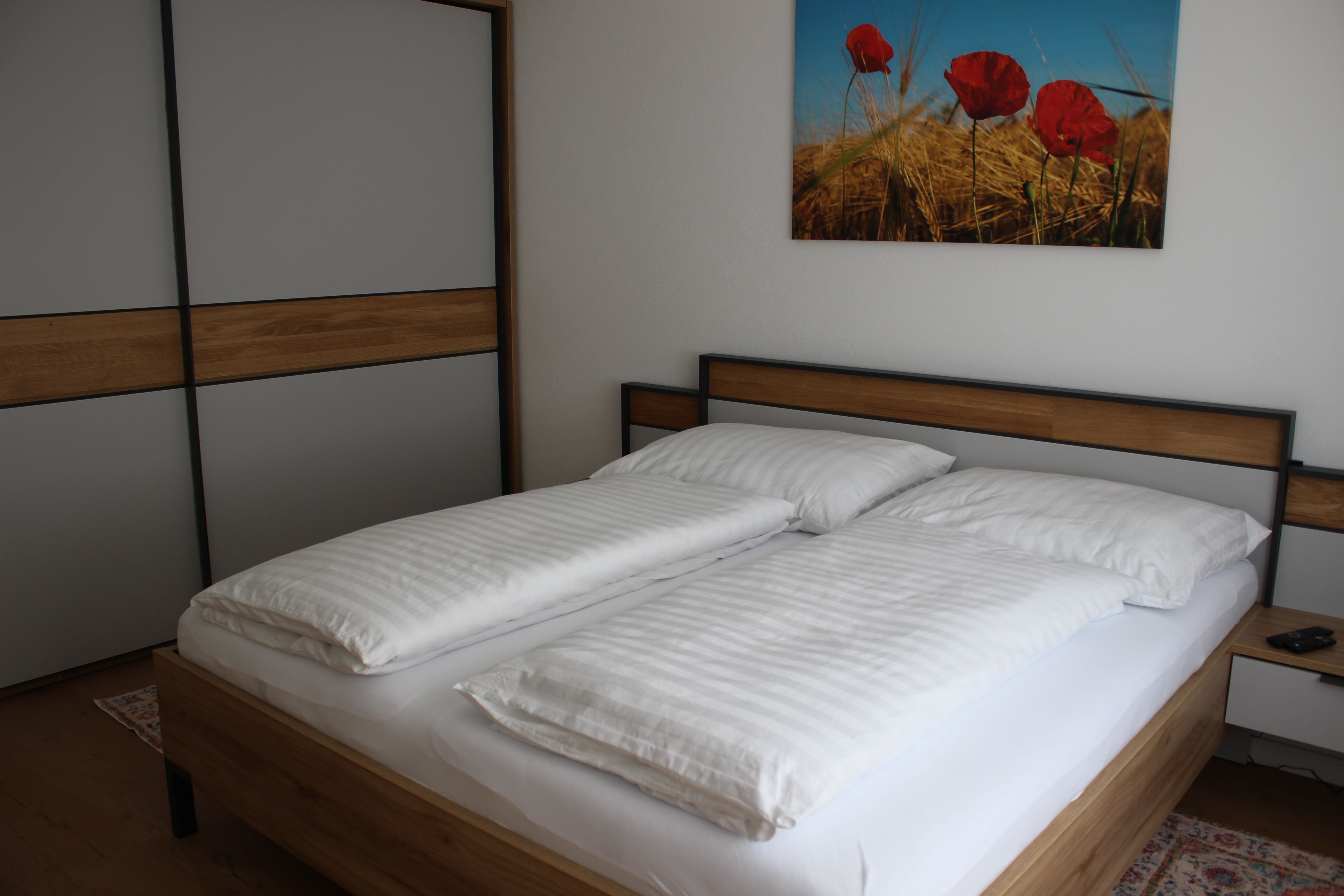 A modern bedroom with a double bed, white comforter covers and a picture of poppies on the wall.