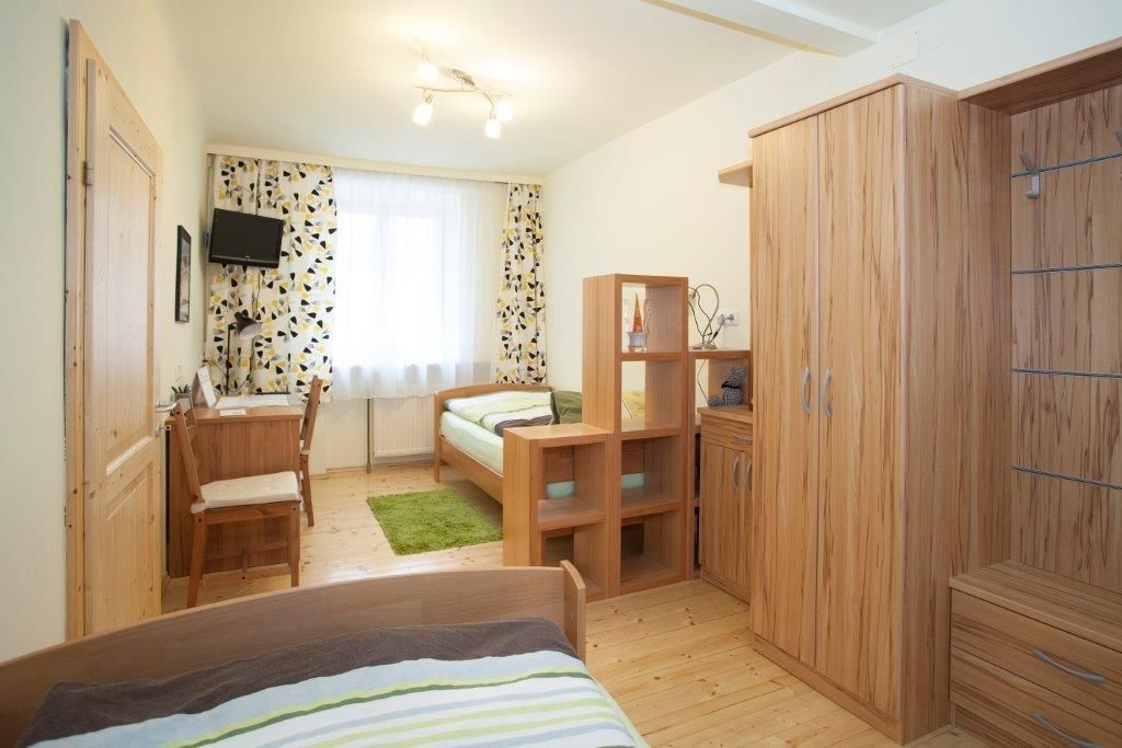 Ein helles Schlafzimmer mit Holzmöbeln, zwei Betten, einem Schreibtisch und einem kleinen Fernseher an der Wand.