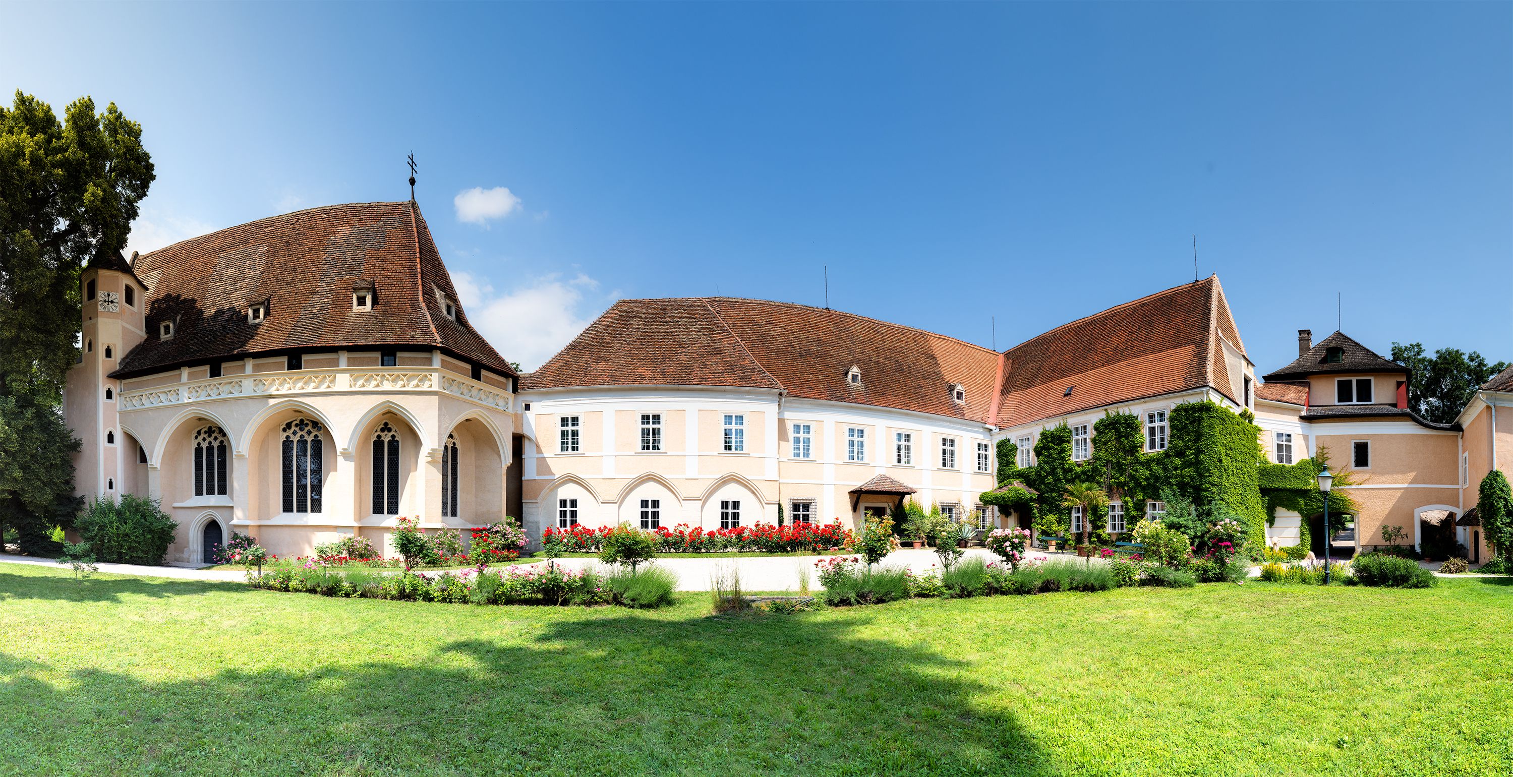 Panoramablick auf das Schloss Schrattenthal mit gepflegtem Garten und blühenden Rosen im Vordergrund.