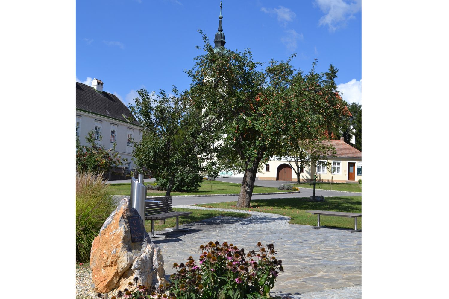 Dorfplatz in Hagenberg mit Kirche, Bäumen und Bänken.