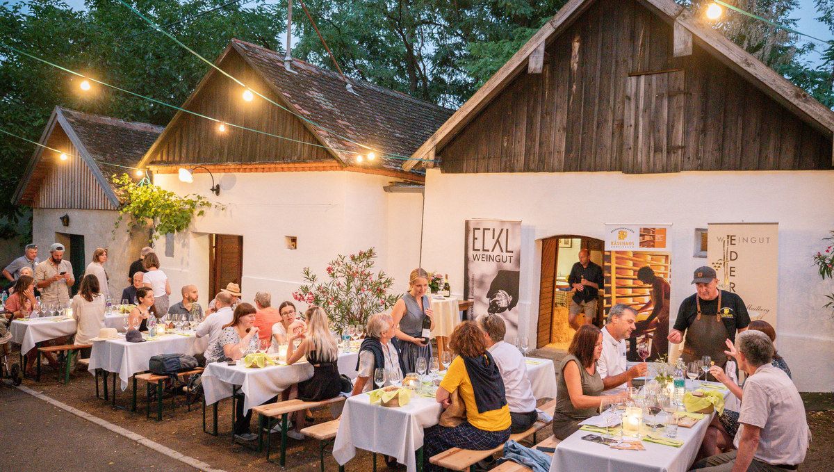 People sit at tables in front of a winery in a wine cellar lane.