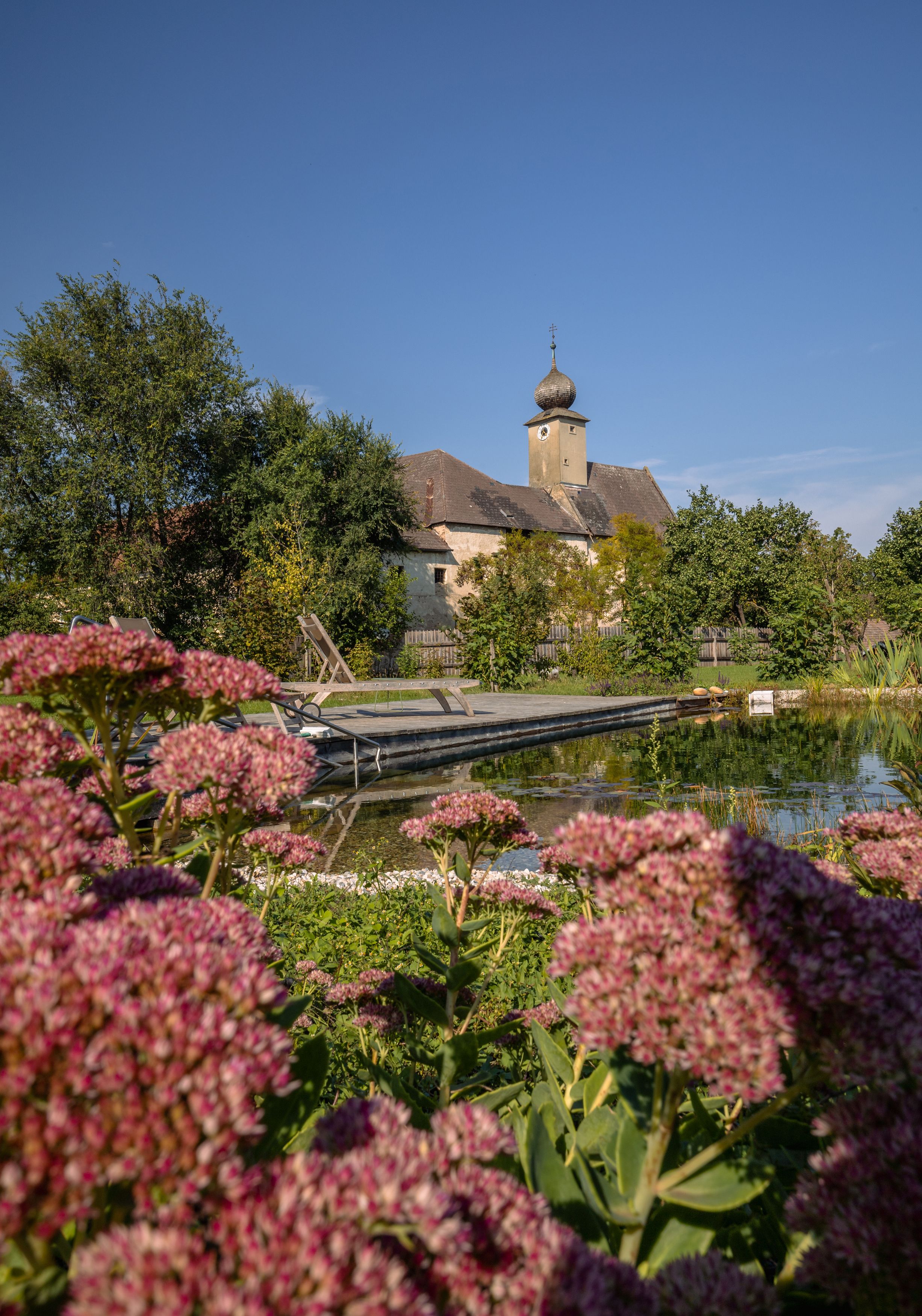 Ein historisches Gebäude mit Zwiebelturm hinter einem Teich und blühenden Pflanzen im Vordergrund.
