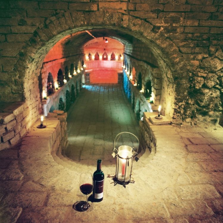 Ein stimmungsvoll beleuchteter Weinkeller mit Kerzen, einer Weinflasche und einem Glas auf einem steinernen Vorsprung.