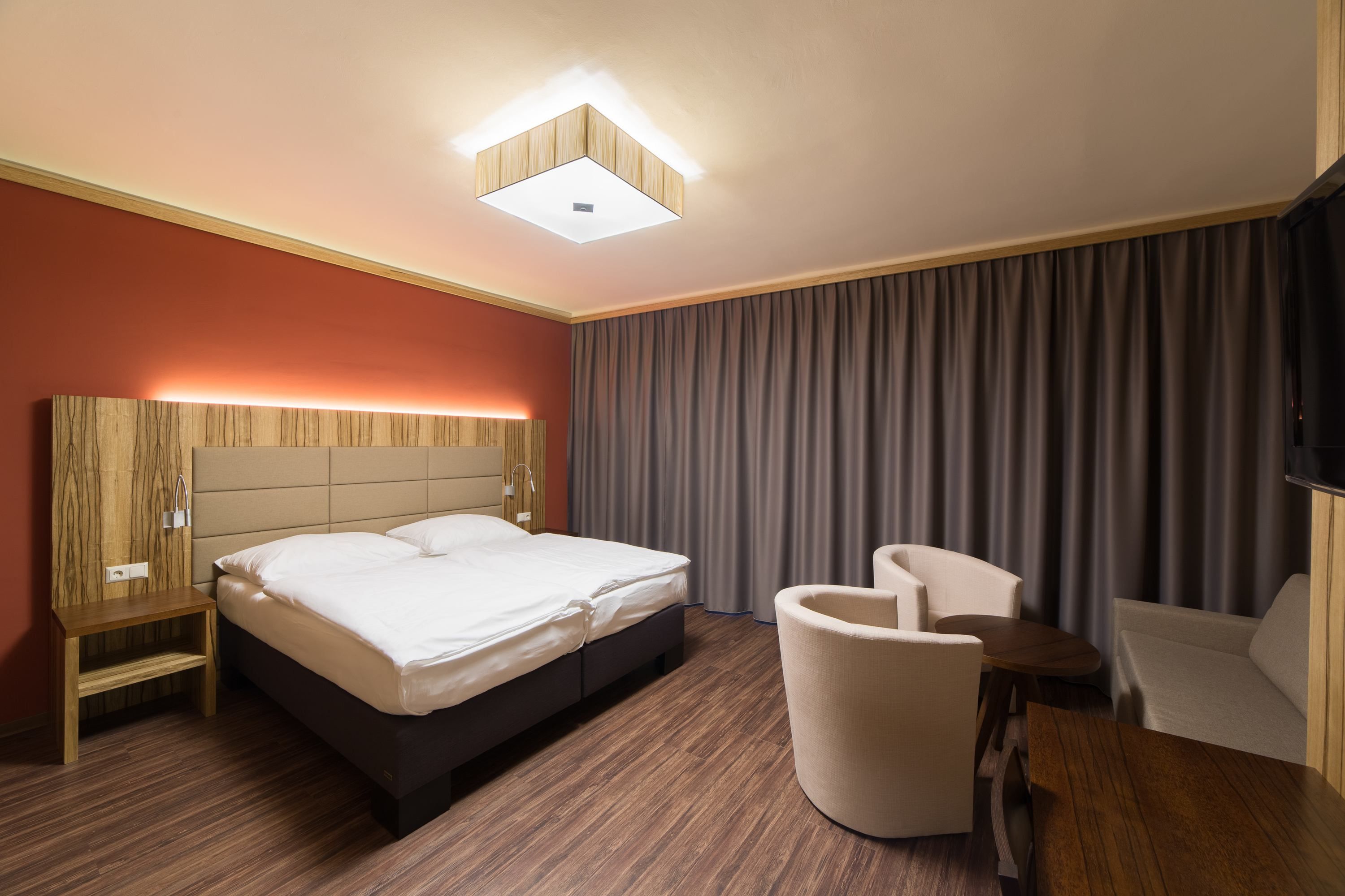 Modern eingerichtetes Hotelzimmer mit Doppelbett, Holzmöbeln und Vorhängen.