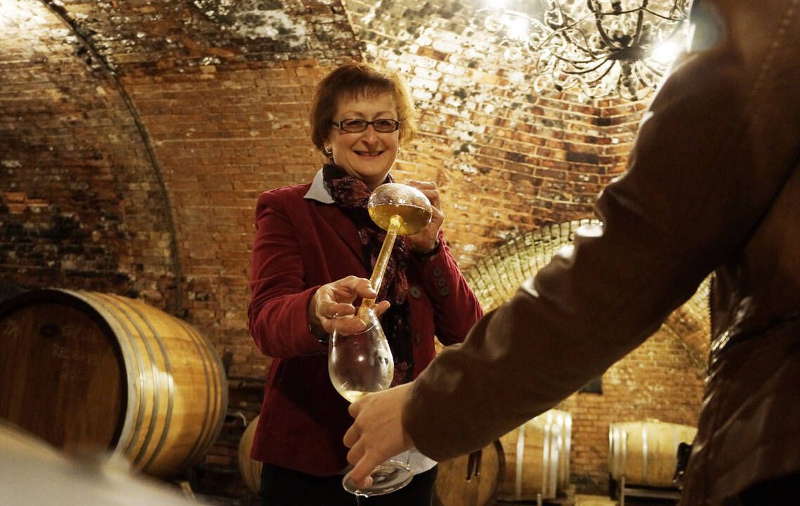 Eine Winzerhin gibt mit einem Weinheber Weißwein in ein Glas.